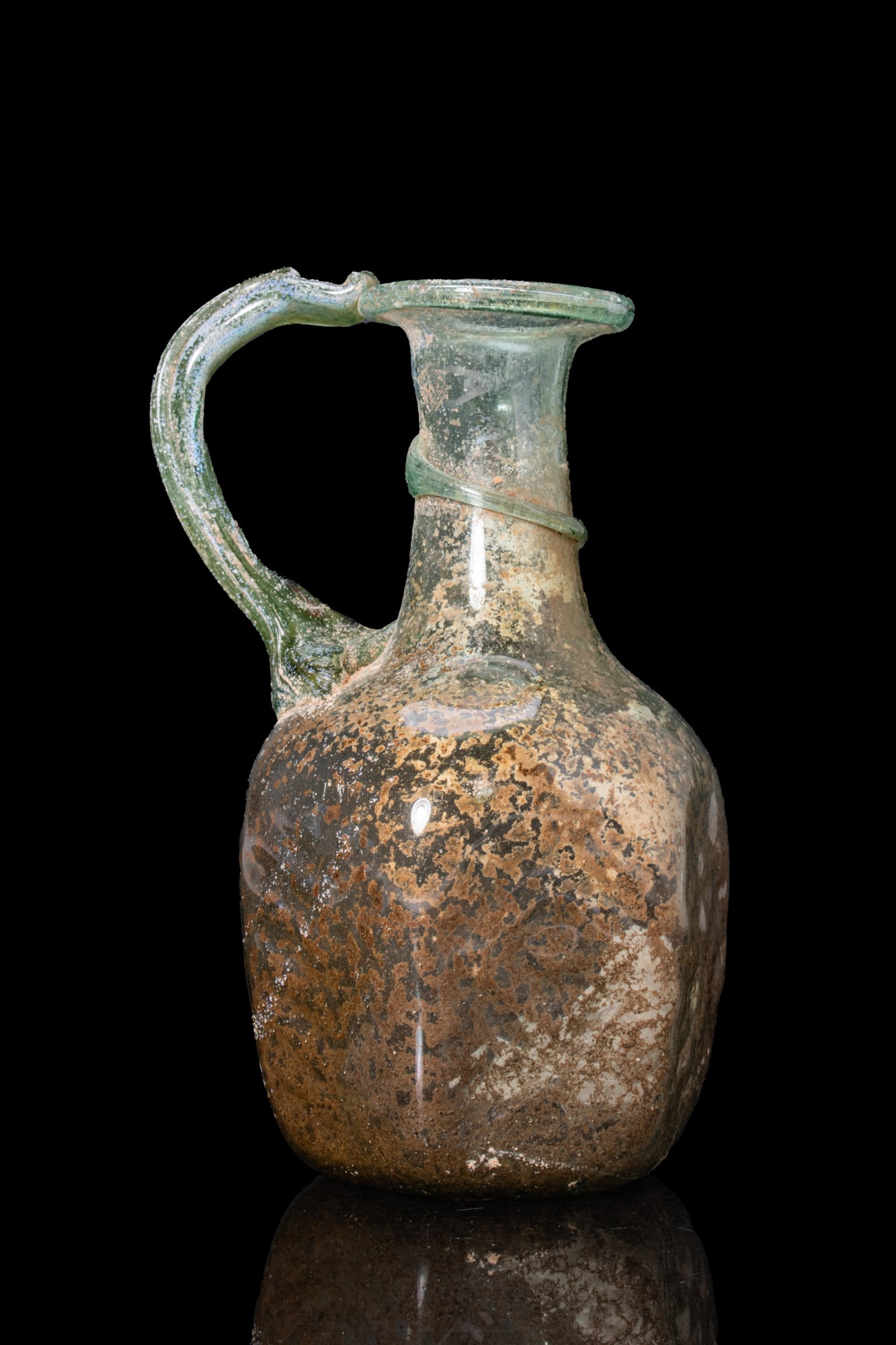 LATE ROMAN GLASS JUG: Ca. AD 300 - 500. A mould-blown hexagonal pale olive green glass jug with a broad folded rim, a short cylindrical neck encircled by an applied trail, and a strap handle extending from the rim to the s