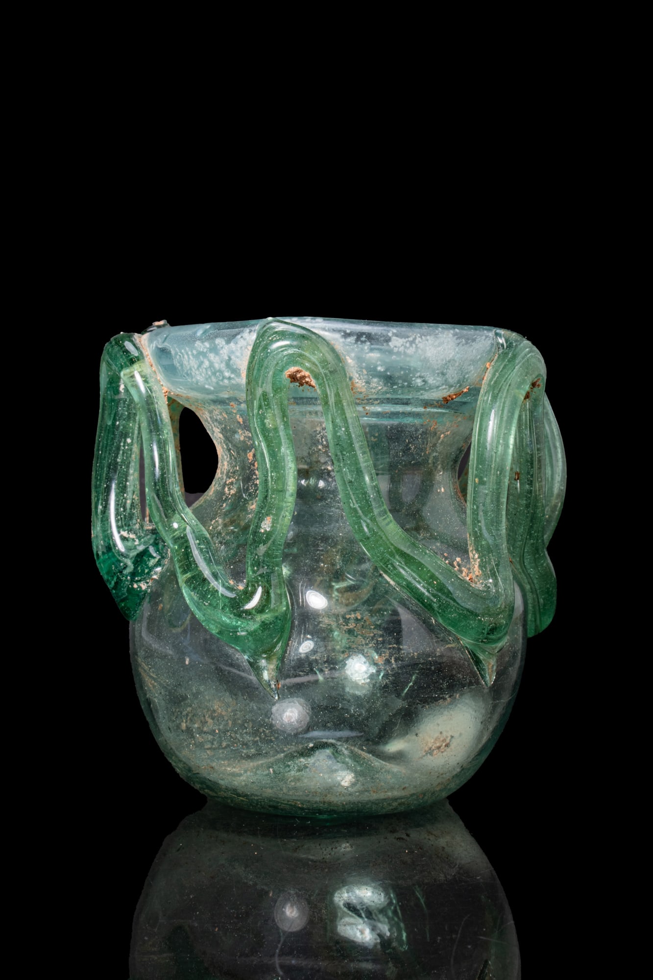 LATE ROMAN GLASS JAR WITH ZIG ZAG MOTIF: Ca. AD 300 - 500. A free-blown translucent pale blue-green glass jar with a rounded body and a short neck below a broad folded rim, decorated with an applied zigzag trail extending from the shoulder t