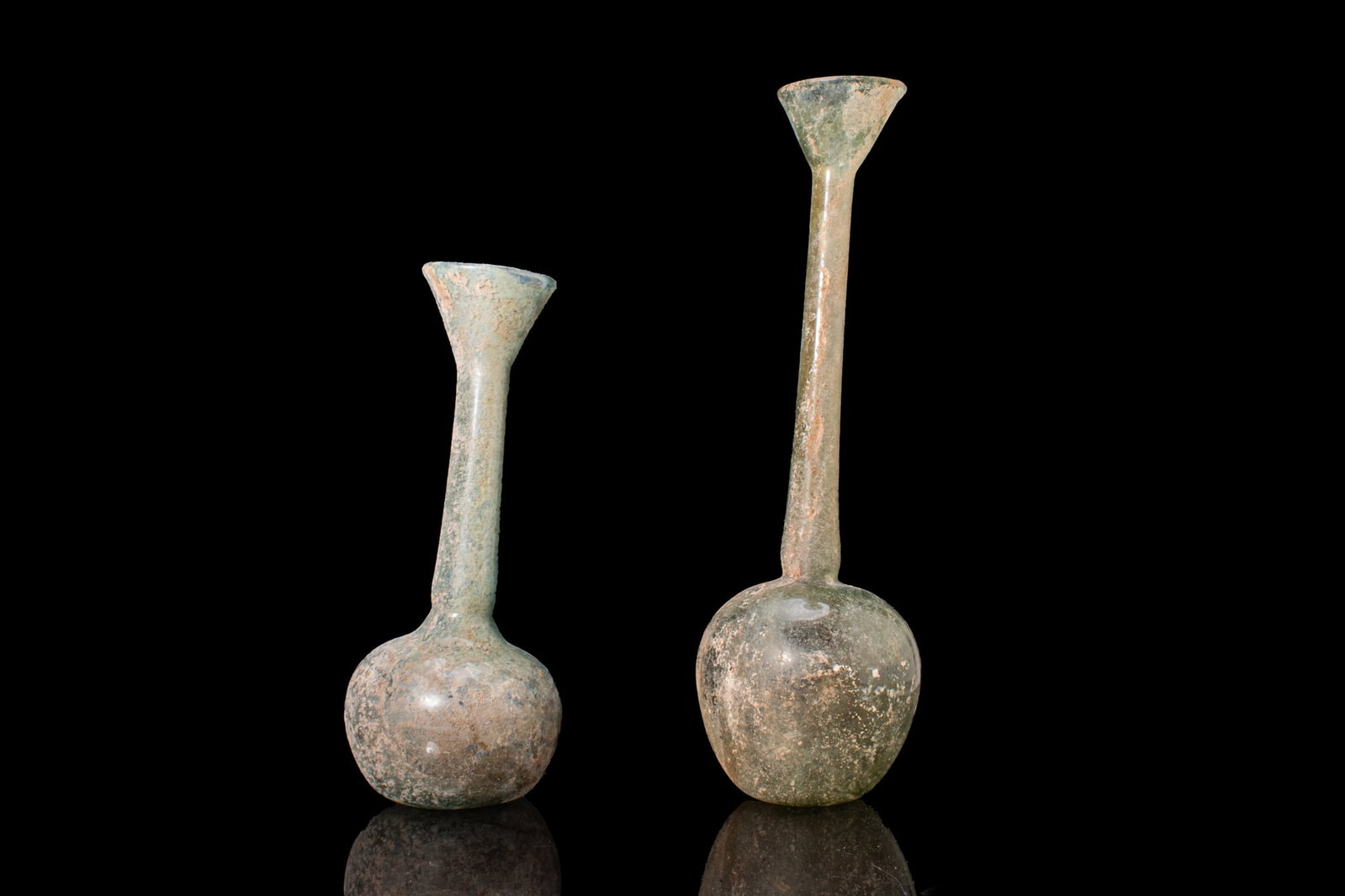 PAIR OF LARGE ROMAN GLASS UNGUENTARIA: Ca. 100 BC - AD 100. A pair of free-blown translucent pale green glass unguentaria, each with a globular body, a long slender neck, and a broad funnel-shaped mouth, set on a slightly concave base. For
