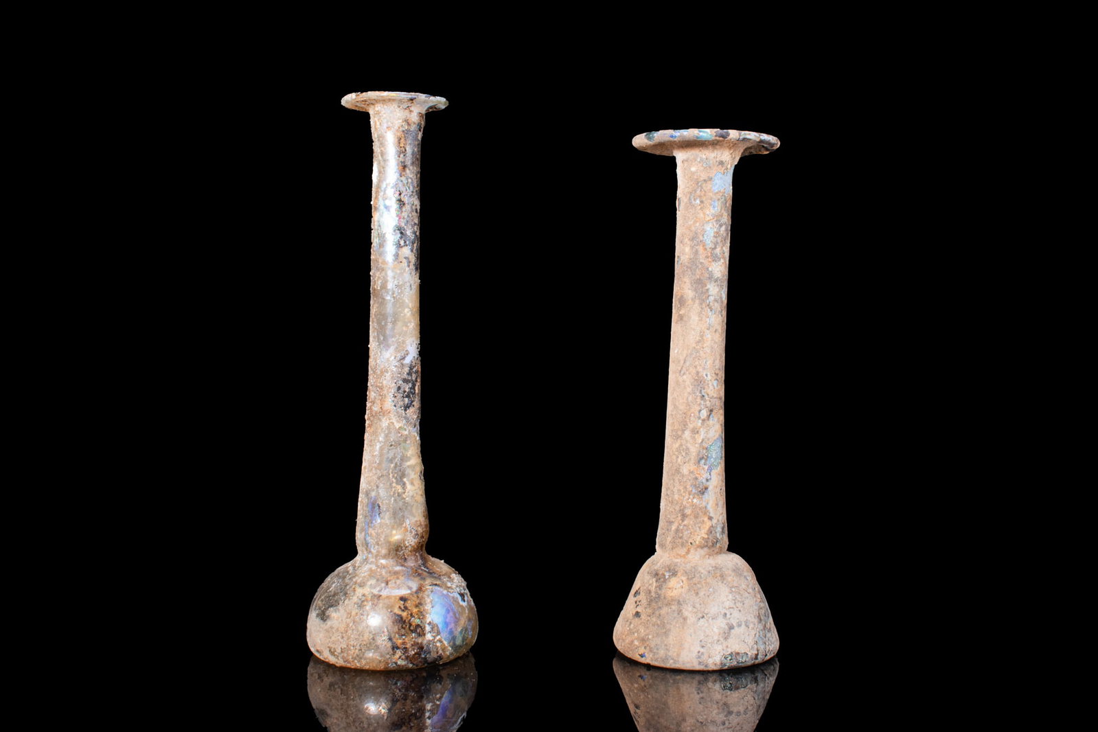 PAIR OF LATE ROMAN GLASS VESSELS: Ca. AD 300 - 500. A pair of free-blown glass vessels, from left to right: a pale blue-green glass jar with a cylindrical body, a short neck, and a funnel-shaped mouth with a collar; and a translucent 