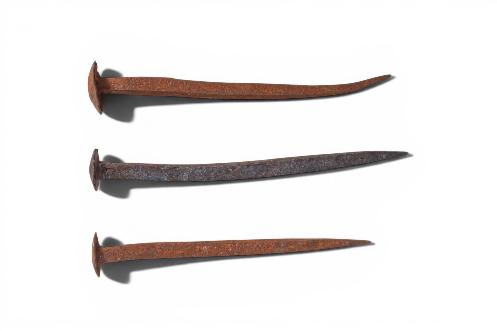 COLLECTION OF ROMAN IRON HAMMERED NAILS: Ca. 100 BC - AD 200. A collection of three iron nails, each with a flat discoid head and a long, straight shank tapering to a sharp point. For similar see: The British Museum, Museum number 1856,1226.