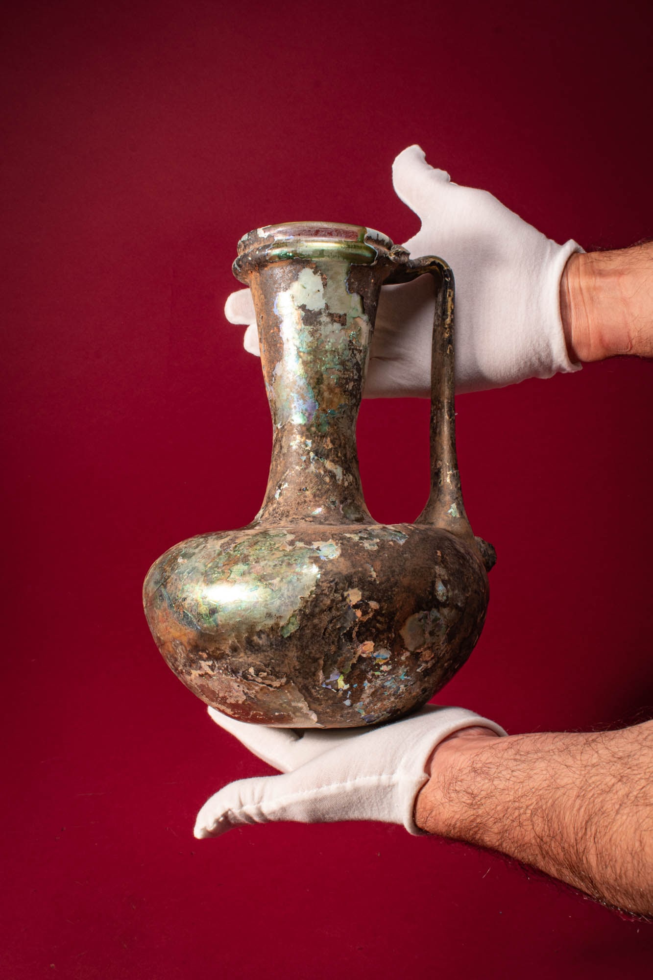 STUNNING MASSIVE LATE ROMAN GLASS JUG: Ca. AD 100 - 300. A free-blown translucent green glass jug with a broad globular body, a tall waisted neck, and a collared mouth. A single strap handle rises from the rim and returns to the shoulder. 