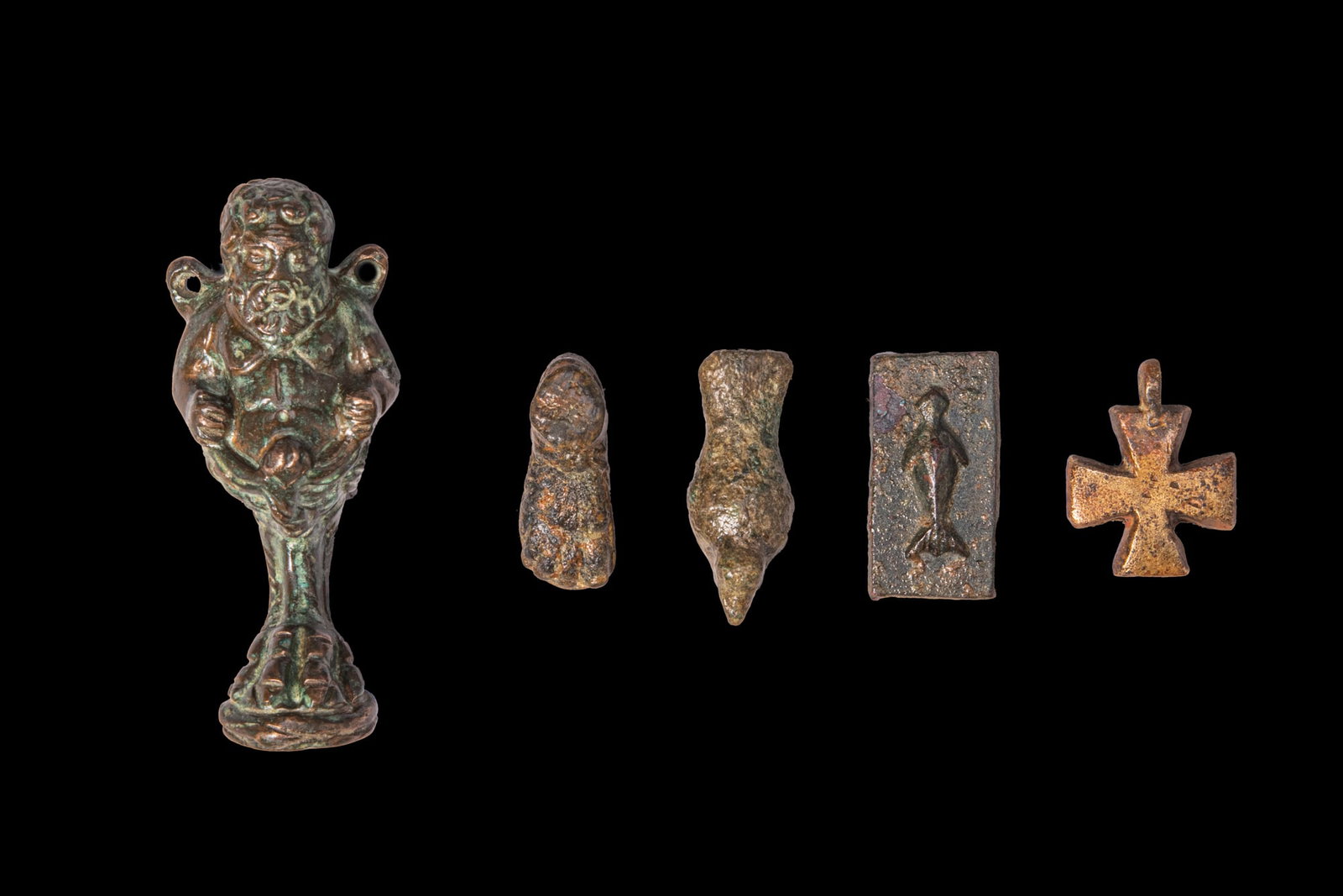 COLLECTION OF ROMAN AND BYZANTINE BRONZE AMULETS: Ca. AD 100 - 300. A collection of five bronze amulets, including, from left to right: a satyr modelled as a standing figure on an integral base with pointed ears, a beard, and suspension loops at the 