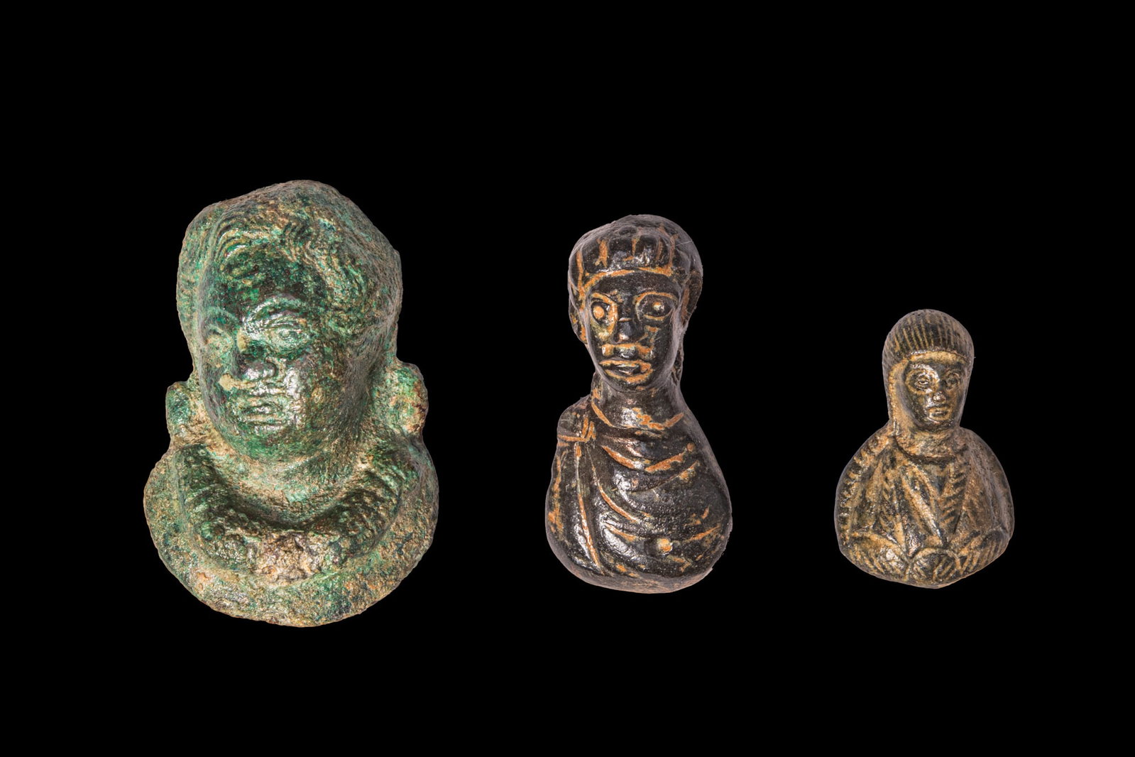COLLECTION OF ROMAN BRONZE BUSTS: Ca. AD 100 - 300. A collection of three bronze busts, including, from left to right: a bust of Cupid with the head slightly tilted, full cheeks, and curly hair; and two busts of emperors, each draped,
