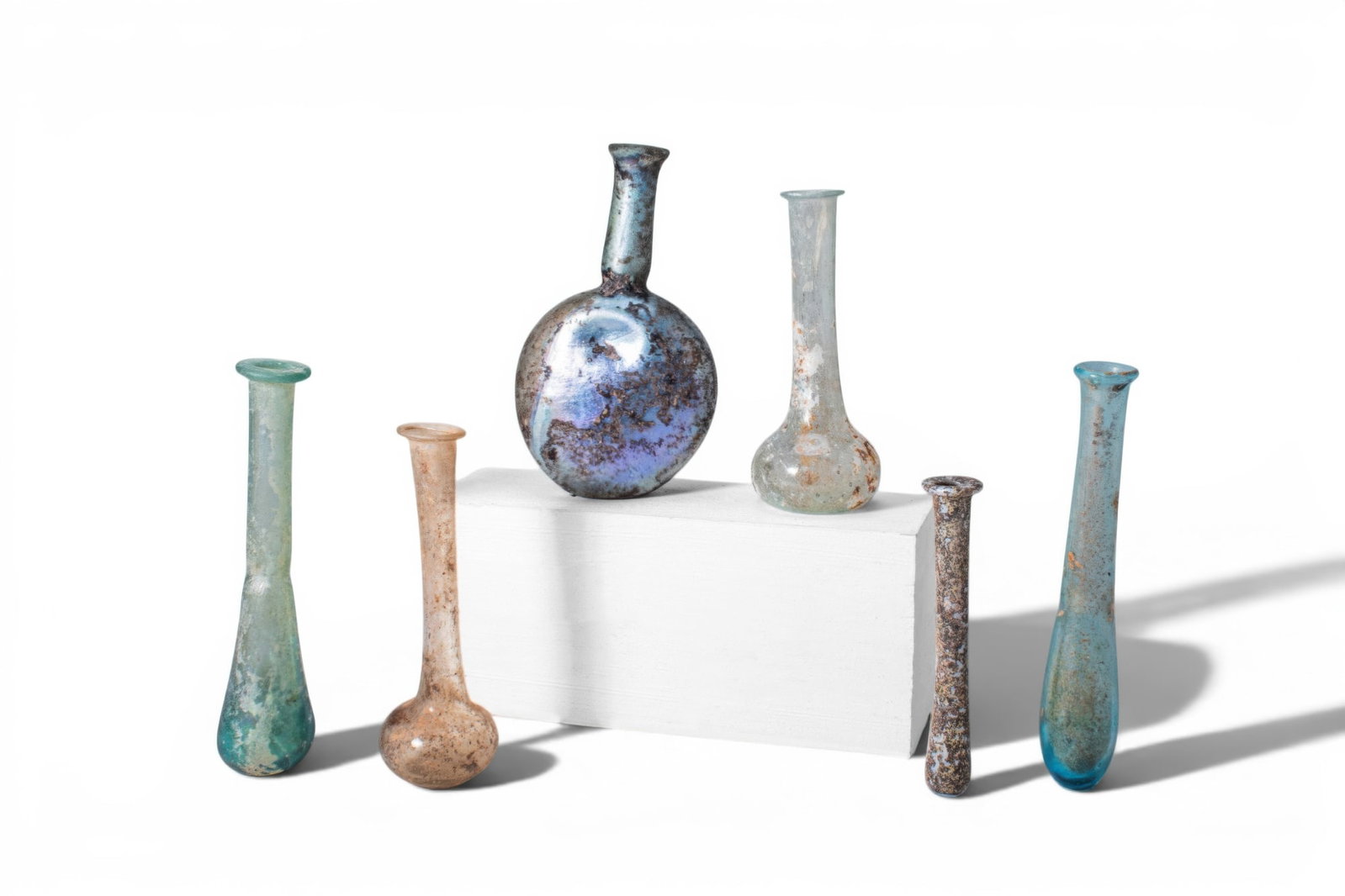 LARGE COLLECTION OF ROMAN GLASS UNGUENTARIA: Ca. AD 1 - 400. A collection of six glass unguentaria, including, from left to right: a bottle with an elongated tear-shaped body and a long cylindrical neck with a folded rim; a bottle with a rounded