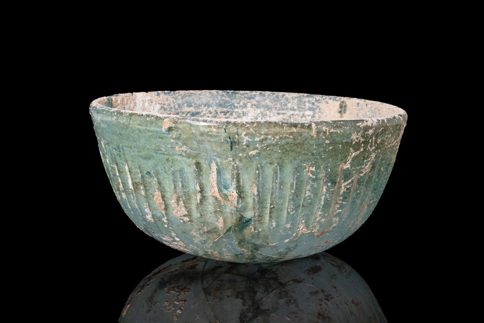 ROMAN PALE BLUE GLASS RIBBED BOWL: Ca. 100 BC - AD 100. A translucent pale blue glass bowl with a deep, flaring body and a thick rim. The exterior is decorated with vertical fluting. For similar see: C. S. Lightfoot, The Cesnola Collec