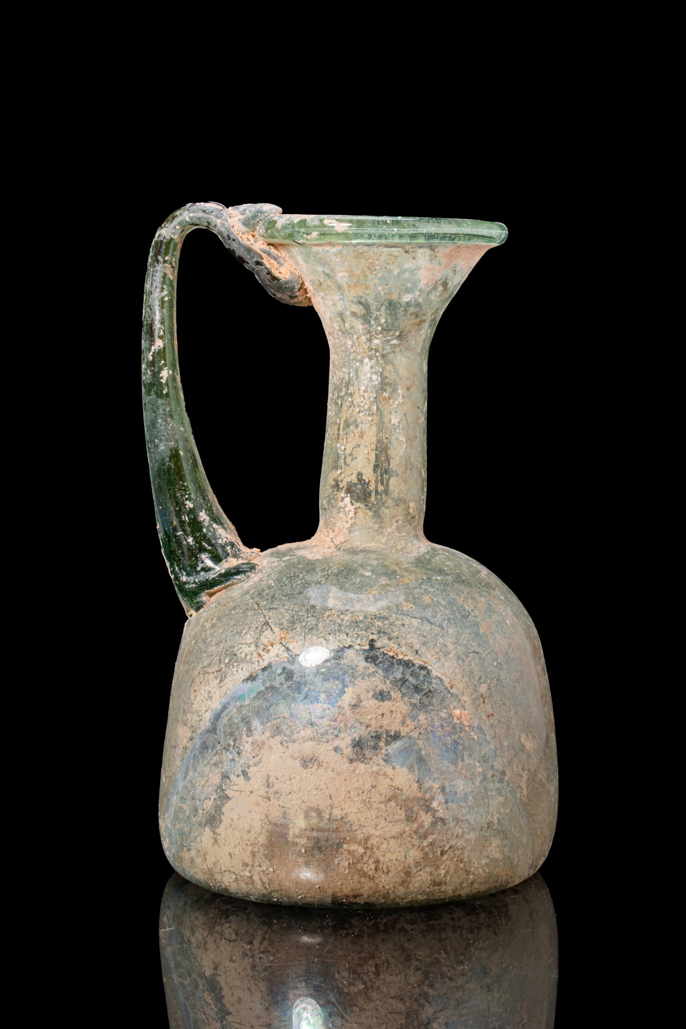 LATE ROMAN GLASS JUG: Ca. AD 300 - 500. A free-blown translucent pale green glass jug with a bell-shaped body, a tall cylindrical neck opening to a flaring mouth, and a bichrome strap handle drawn from the rim to the shoul