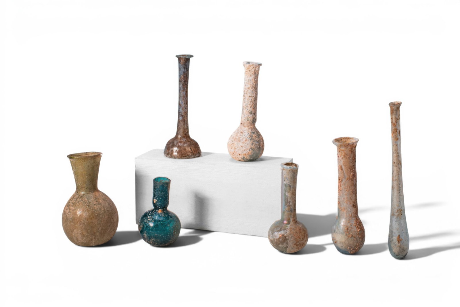 LARGE COLLECTION OF ROMAN GLASS UNGUENTARIA: Ca. AD 1 - 400. A collection of seven glass unguentaria, including, from left to right: a bottle with a squat globular body and a funnel-shaped neck; a bottle with a spherical body and a short cylindr