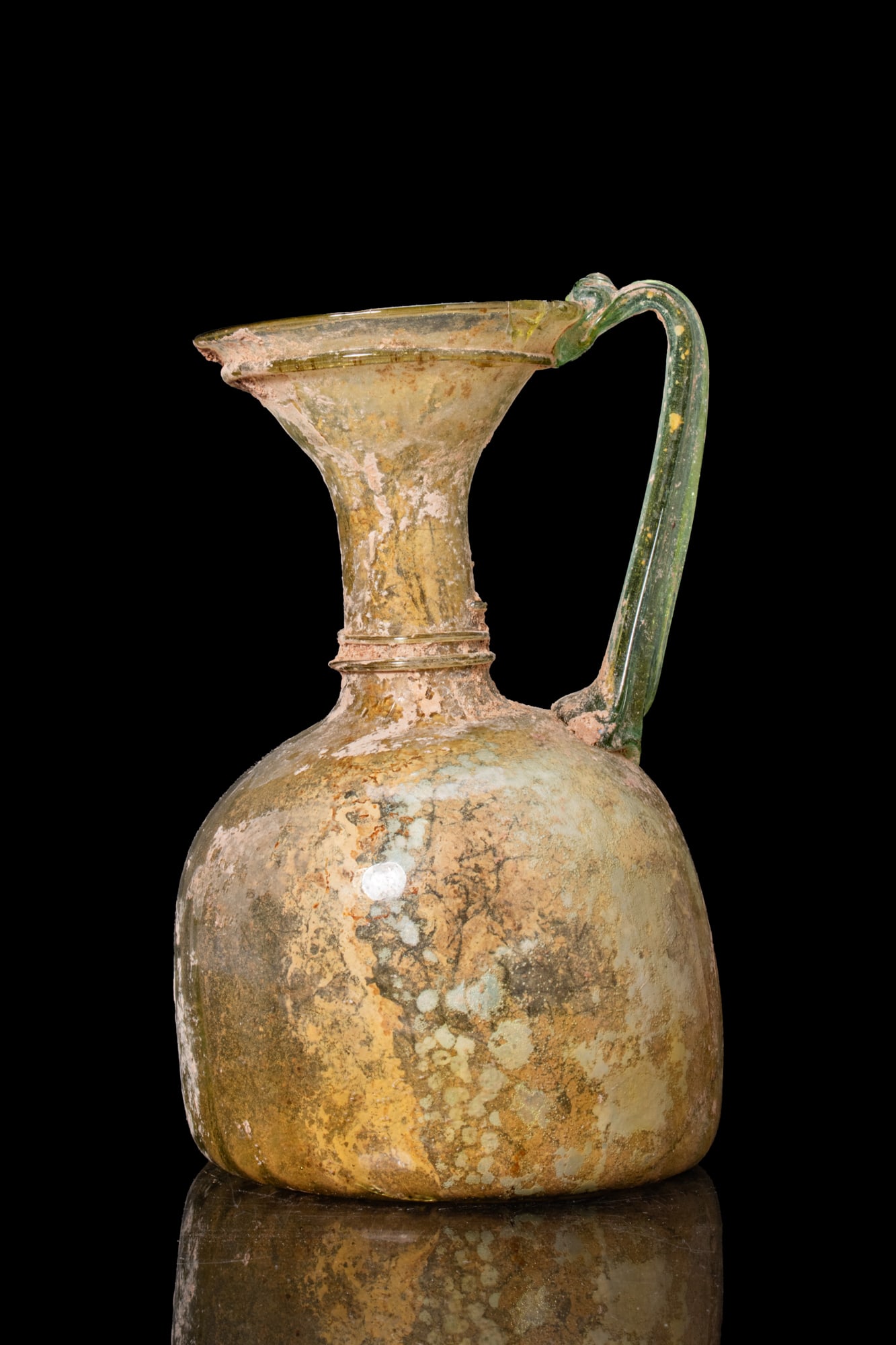 LATE ROMAN GLASS JUG: Ca. AD 300 - 400. A bichrome free-blown glass jug with a translucent amber body and a green strap handle drawn from the rim to the shoulder. The vessel has a bell-shaped body, a cylindrical neck, and 