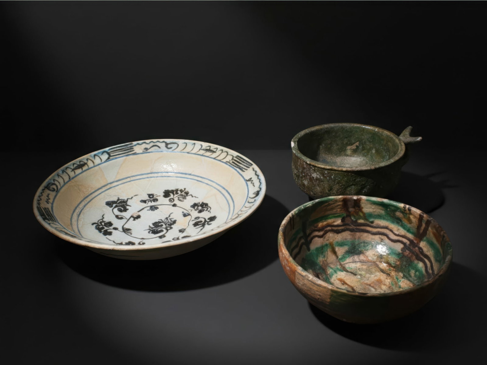 COLLECTION OF ISLAMIC GLAZED TERRACOTTA BOWLS: Ca. AD 1400 - 1700. A collection of three pottery bowls, including, from left to right: a large shallow bowl with a broad open well, painted in black and blue on a cream ground with a central roundel 
