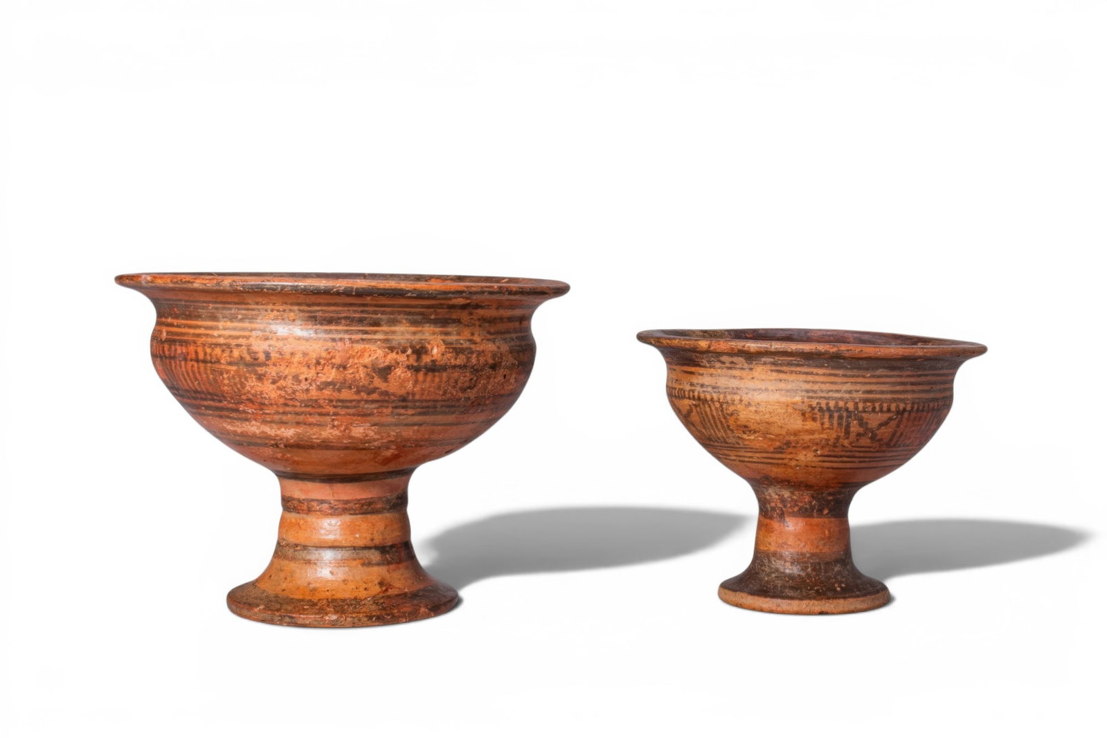 PAIR OF INDUS VALLEY CHALICES WITH GEOMETRIC DECORATION: Ca. 2500 - 2200 BC. A pair of pottery chalices, each with a deep, rounded bowl on a tall trumpet foot and a broad everted rim. Both are decorated with linear ornament around the exterior, including ha