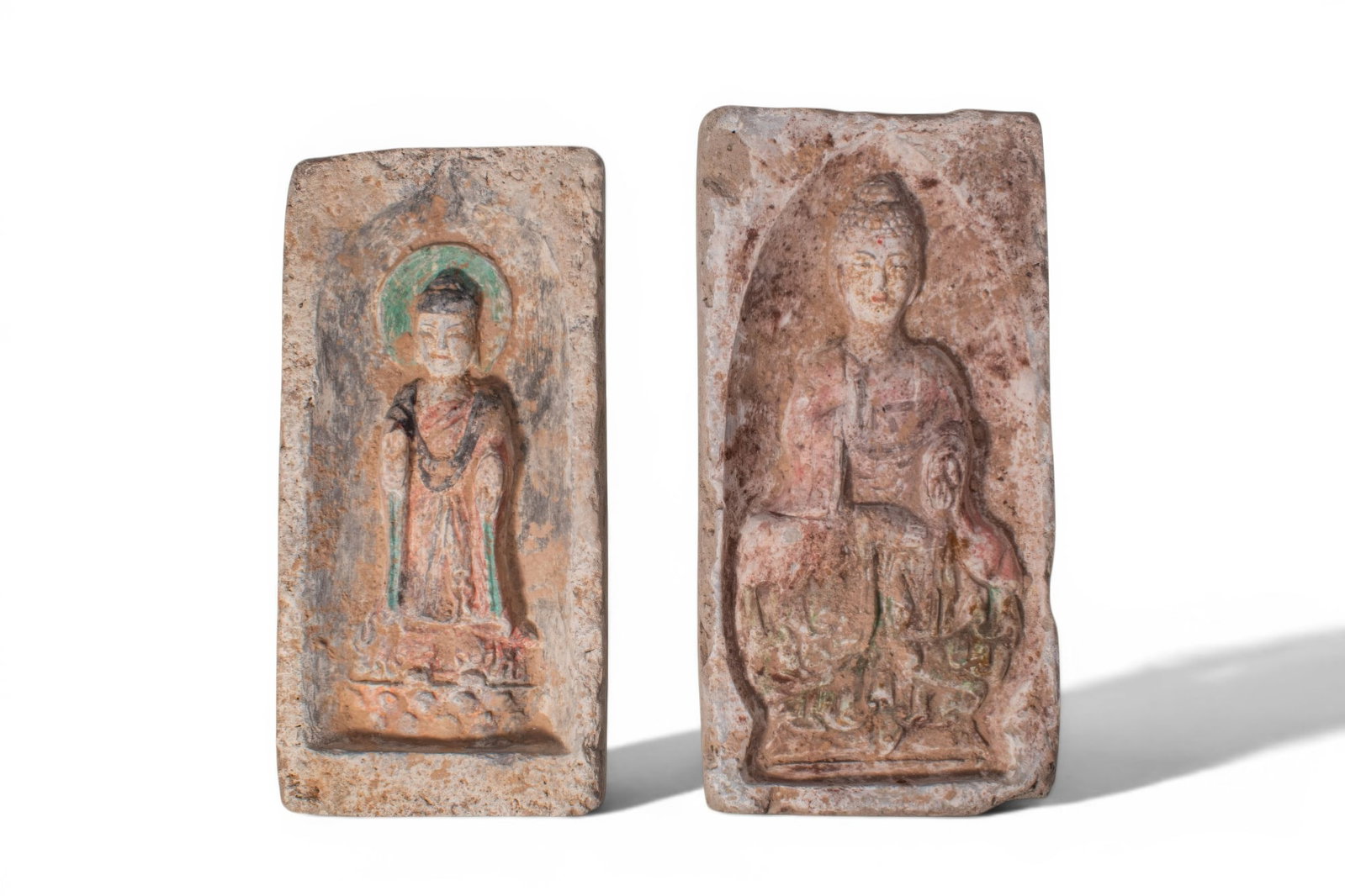 PAIR OF CHINESE NORTHERN WEI TERRACOTTA BUDDHIST TILES: Northern Wei dynasty, Ca. AD 386 - 534. A pair of rectangular terracotta tiles, from left to right: a tile with a standing Buddha set within a recessed niche and backed by a green halo, wearing a long