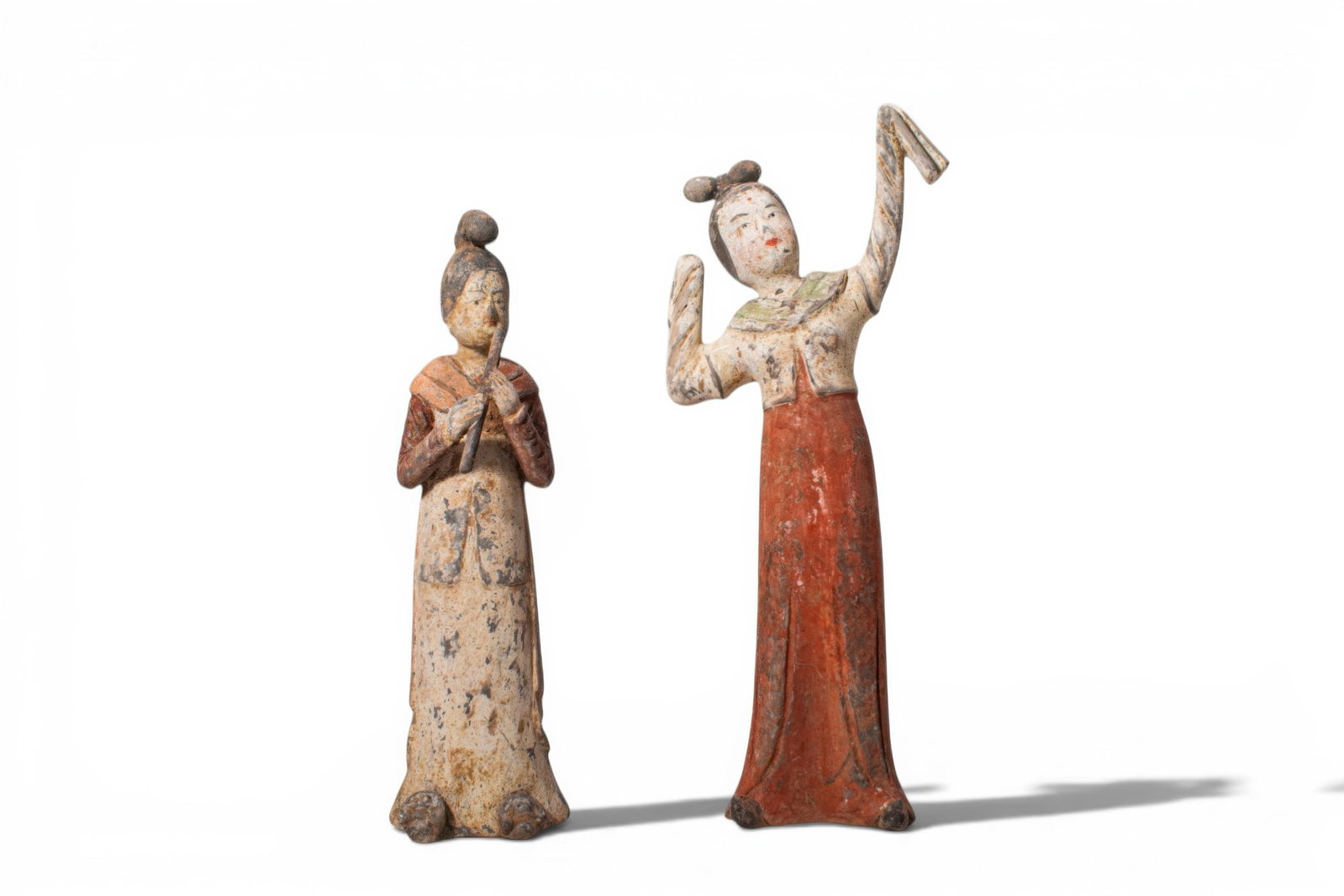 PAIR OF CHINESE TERRACOTTA FEMALE FIGURES, MUSICIAN AND DANCER: Tang dynasty, Ca. AD 618 - 907. A pair of terracotta female figures, including, from left to right: a standing musician in a pale robe with red sleeves and shawl, holding a flute in both hands before 