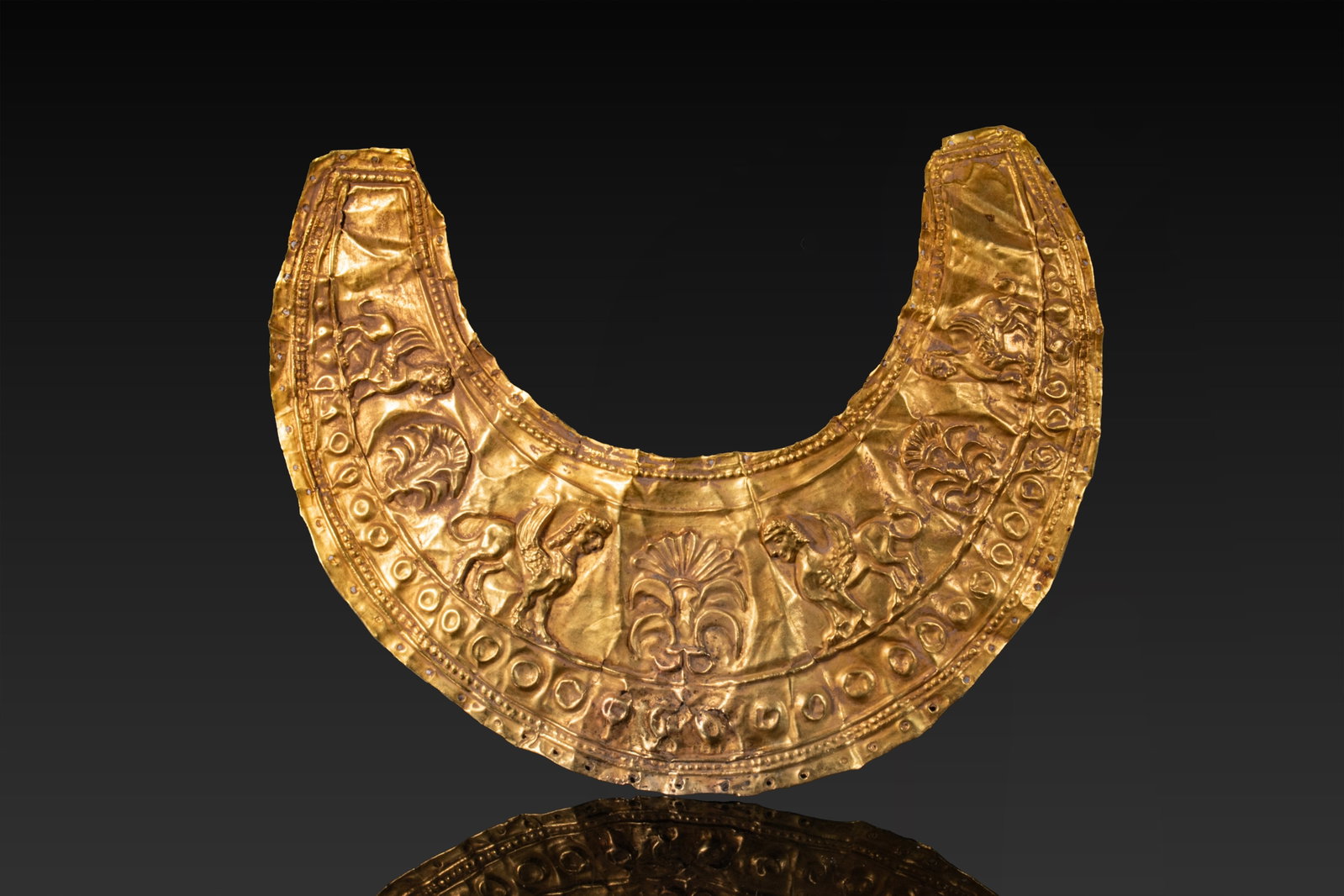 STUNNING GREEK GOLD LEAF PECTORAL WITH SPHINXES AND PALMETTES: Ca. 500 - 300 BC. A broad crescentic pectoral formed from thin gold sheet and decorated in repousse. Raised ribs, beaded bands and a row of circular bosses frame the principal register, which depicts 