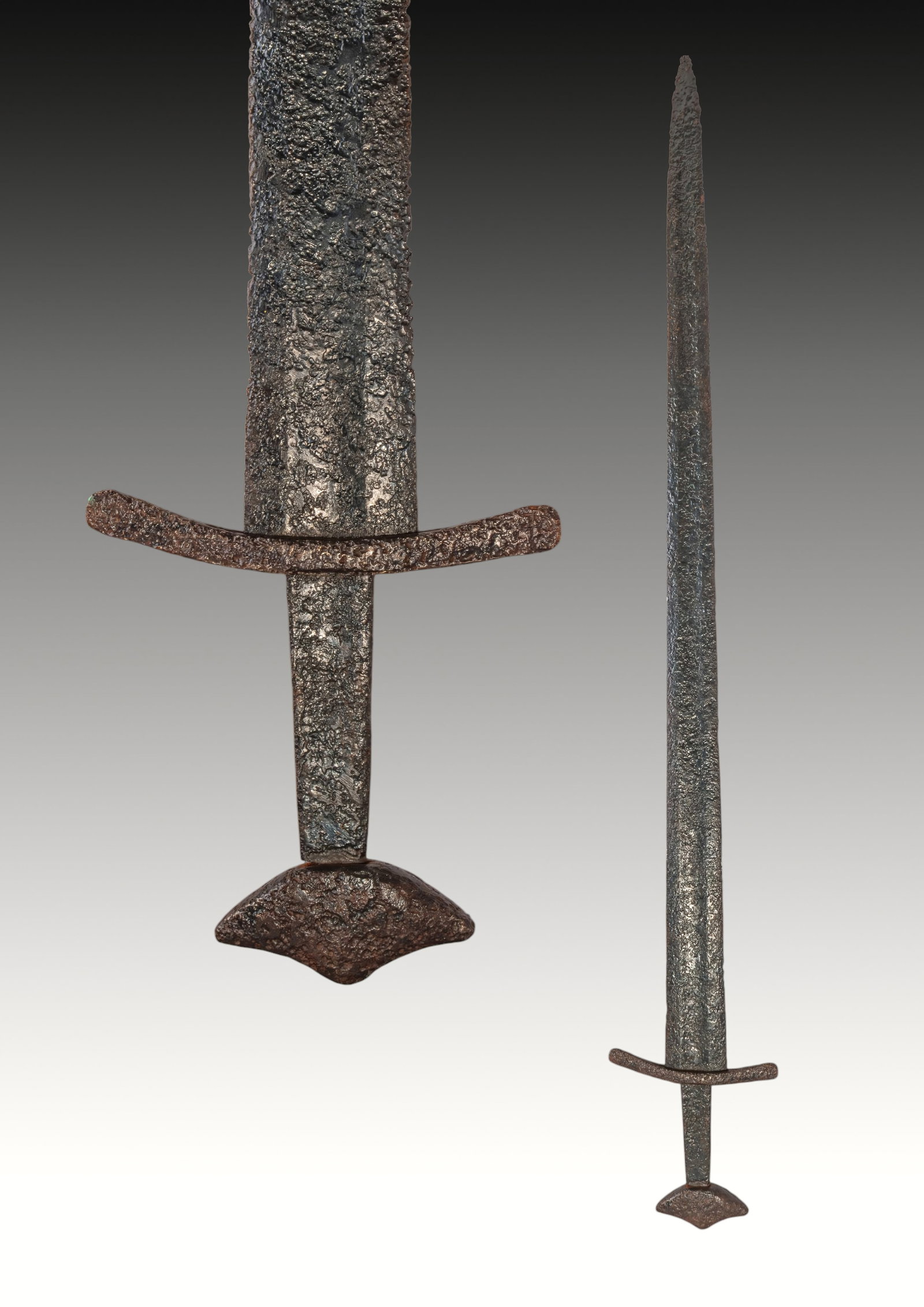 MEDIEVAL VIKING PERIOD IRON SWORD WITH LARGE POMMEL: Ca. AD 1100 - 1300. An iron sword with a long, straight double-edged blade tapering to a pointed tip, with a shallow central fuller extending along the length. A curved crossguard with rounded termina