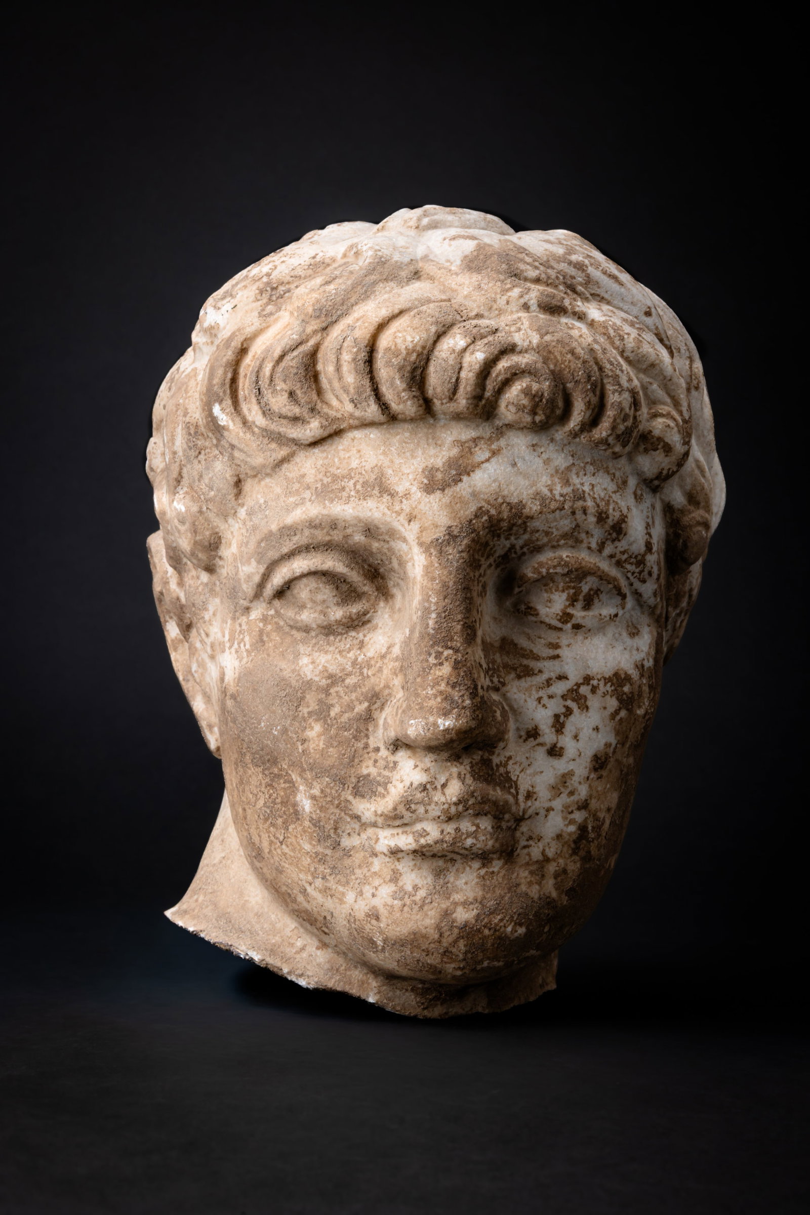 ROMAN MARBLE HEAD OF YOUNG NERO: Ca. AD 1 - 100. A marble portrait head of the young Nero, with the head turned slightly to his left. The face is full, with a rounded chin, prominent eyes and a compact mouth. His thick hair is arrang