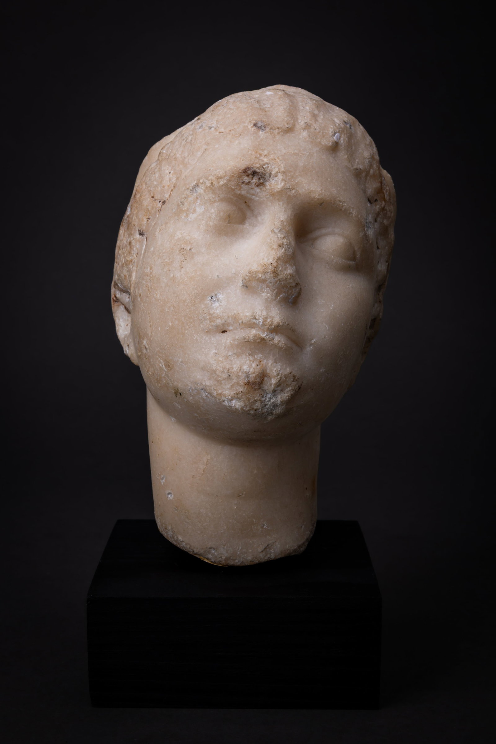 EASTERN ROMAN MARBLE HEAD OF YOUNG WOMAN: Ca. 100 BC - AD 100. A white marble fragment carved as the head of a woman, with waved curls at her forehead divided by a double twisted-rope headband and ending in rows of curls gathered at the base 