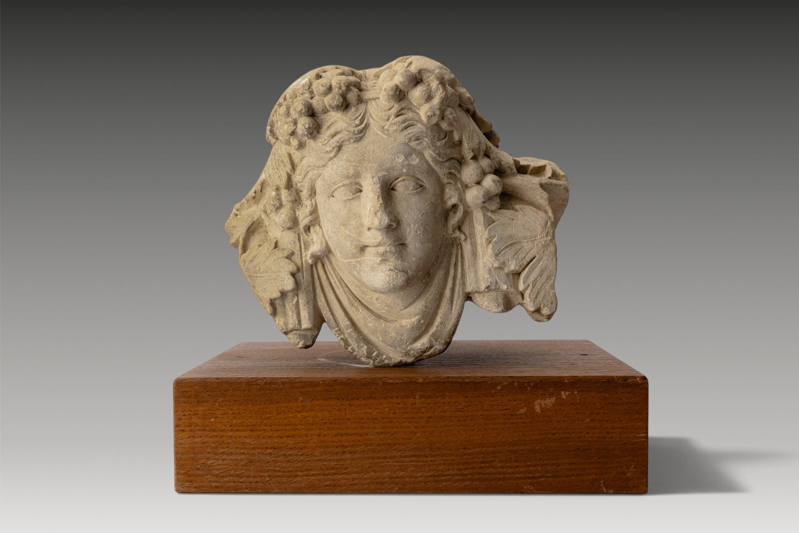 ROMAN STONE RELIEF PANEL OF YOUNG DIONYSUS: Ca. AD 1 - 200. A stone relief panel with the head of young Dionysus. His youthful face is carved with full cheeks, heavy-lidded eyes, a broad nose, small lips and a rounded chin. Long wavy tresses de