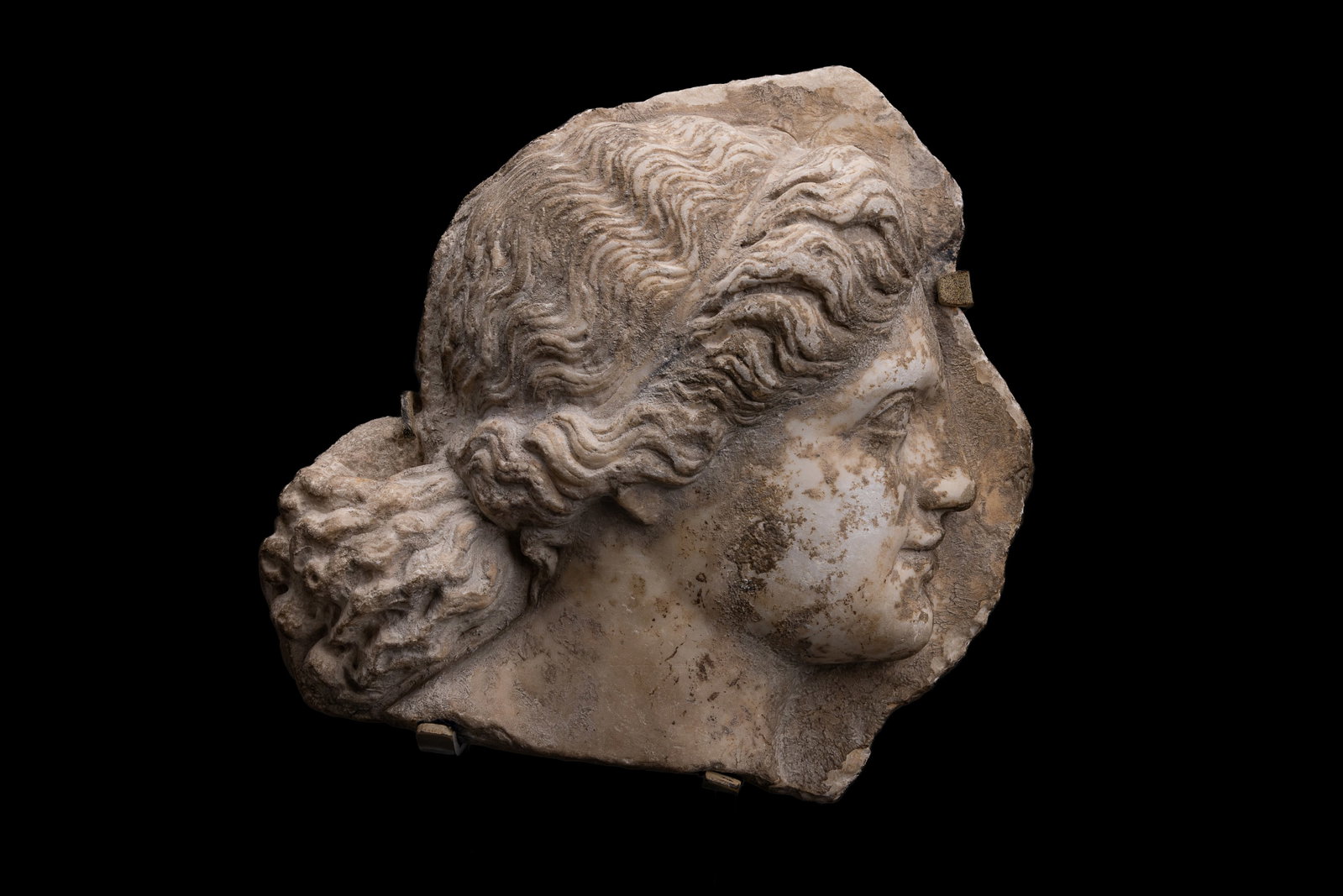 ROMAN BAS-RELIEF MARBLE PANEL OF A HEAD IN PROFILE: Ca. AD 1 - 100. A white marble panel depicting the head and neck of a young maiden in profile, with an archaic smile and her gaze directed forward. Her hair is held by a flat headband and gathered at 