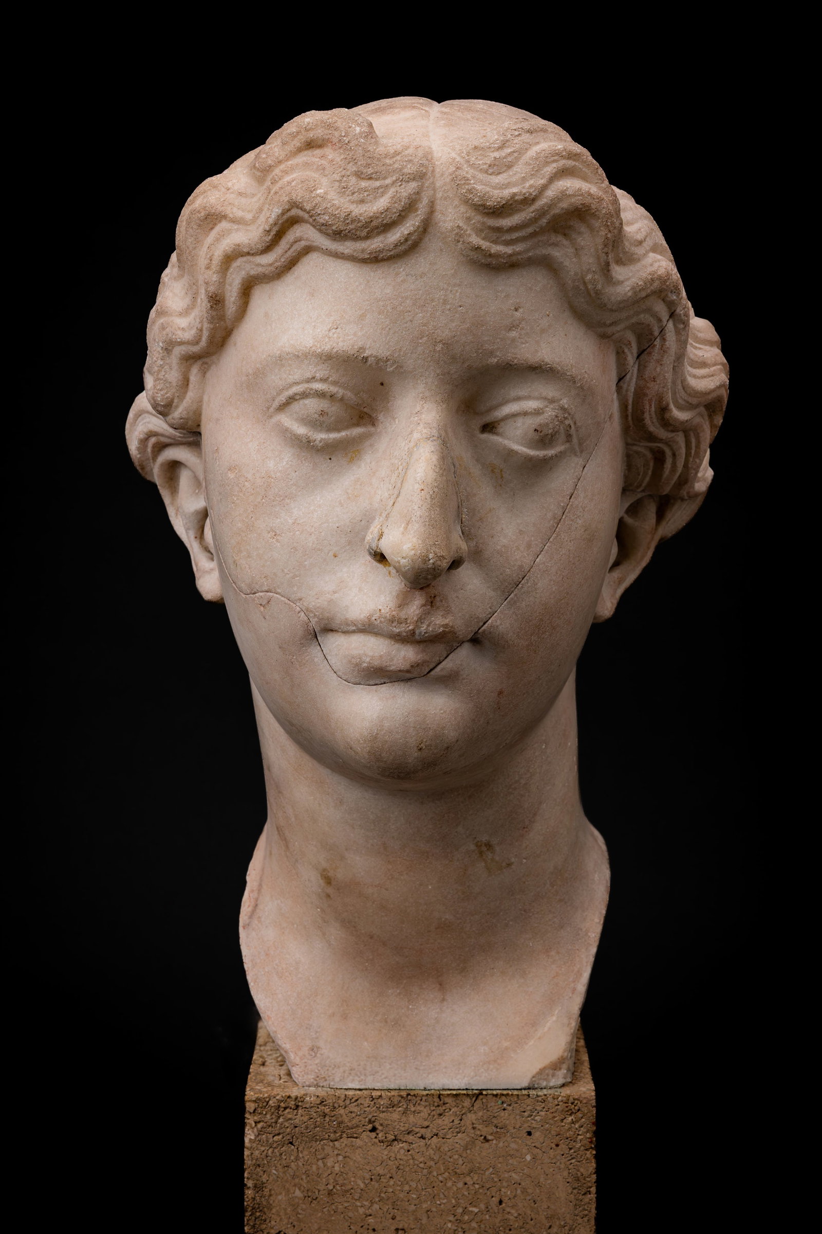 RARE ROMAN MARBLE HEAD OF LIVIA: Ca. AD 14 - 37 . A marble portrait head of Livia with the face turned slightly to the side. Her hair is centrally parted, arranged in broad undulating locks across the forehead and temples, and drawn 