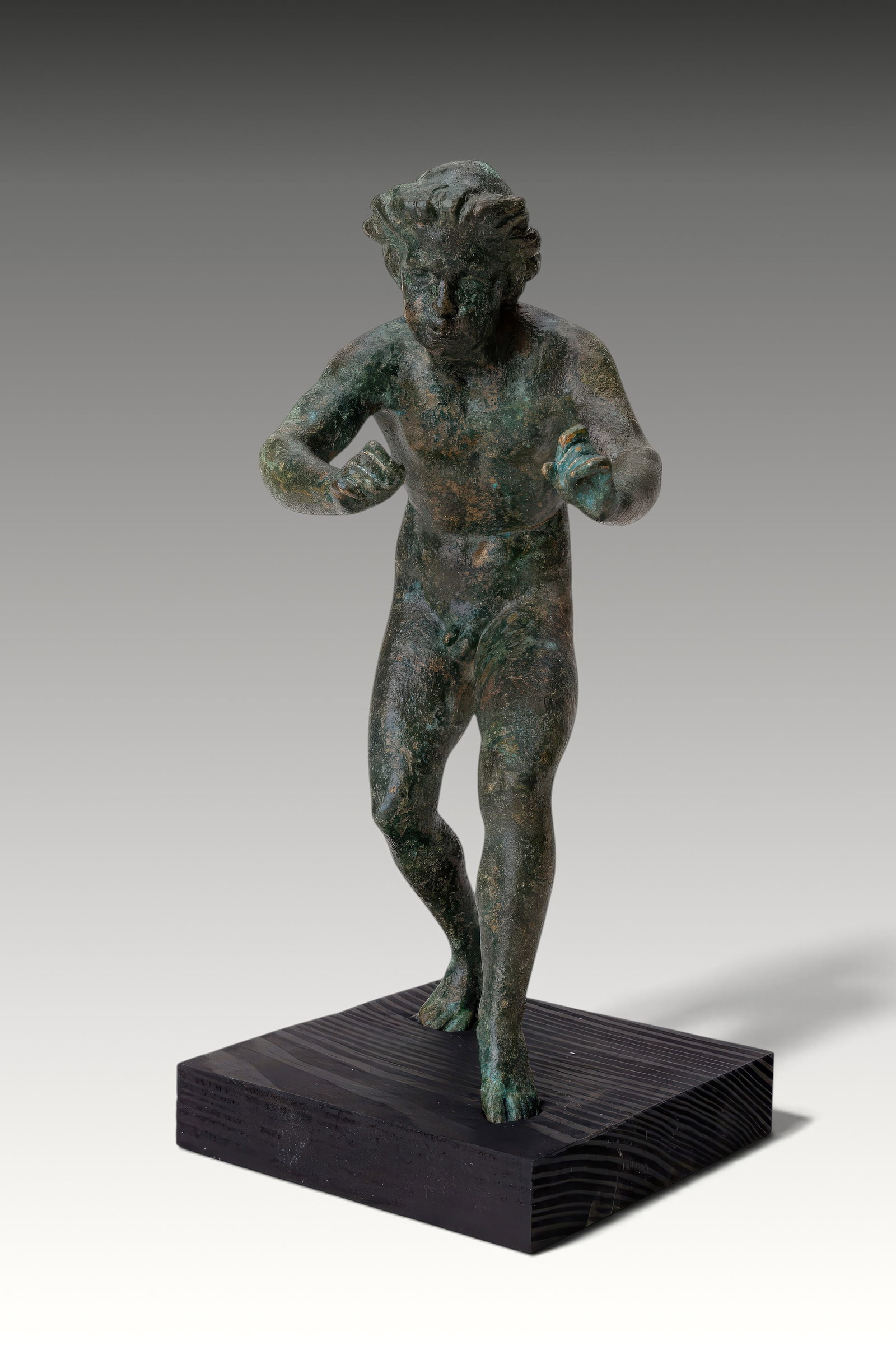 RARE ROMAN BRONZE FIGURINE OF A MUSICIAN PLAYING A FLUTE: Ca. AD 100 - 300. A cast bronze figurine of a musician with the left leg extended and the right leg drawn back. The nude figure leans slightly forward, with both arms bent and the hands raised before 