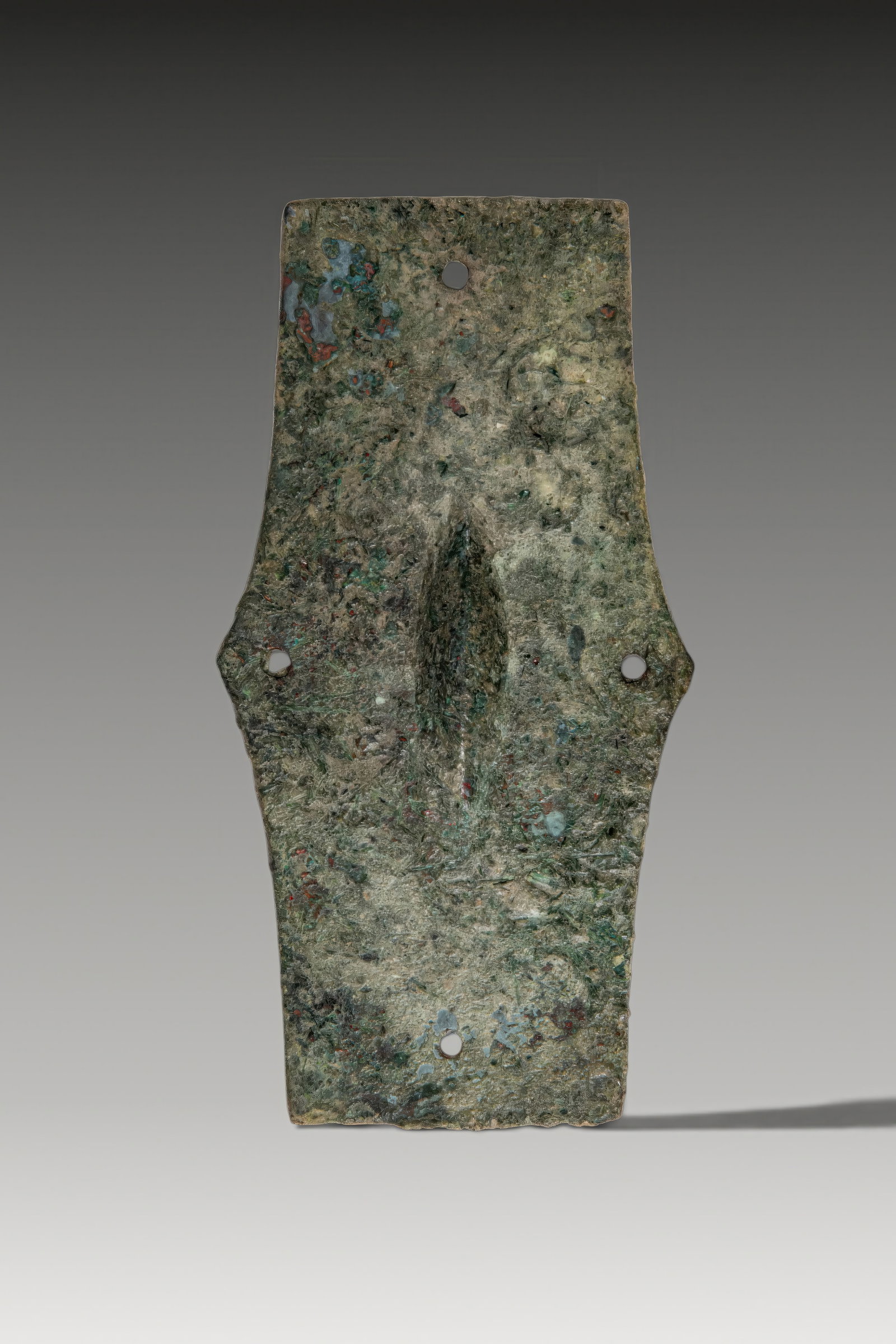 CELTIC BRONZE UMBO: Ca. 500 BC. A bronze umbo with an elongated plate, angular projections at the centre of the upper and lower edges, a central boss, and four perforations near the margins for attachment. For similar se