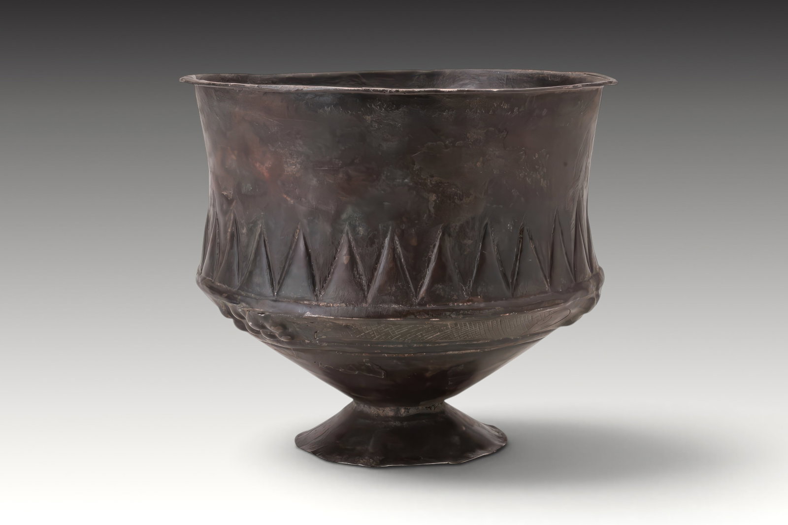 URARTIAN SILVER CUP WITH BAND OF TRIANGLES: Ca. 1200 - 900 BC. A silver cup standing on a flared foot, with a conical lower body and deep cylindrical bowl opening to a broad mouth and flat out-turned rim. The main body is decorated with an inci