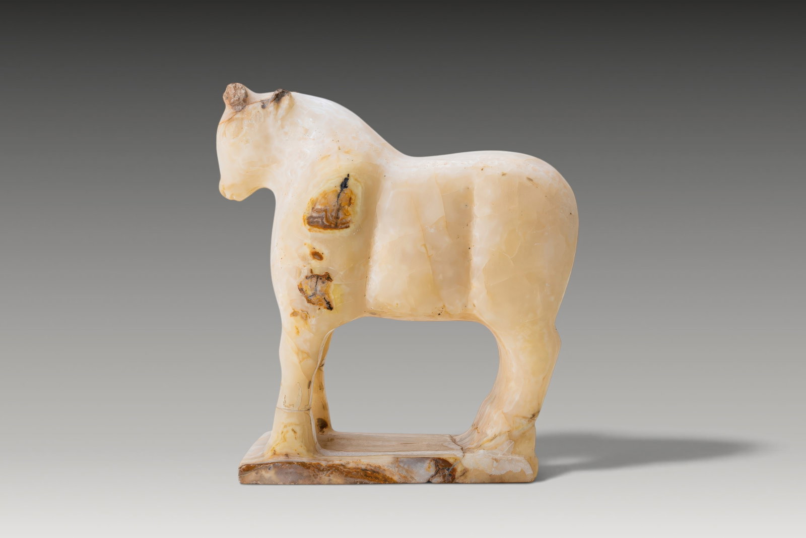 SOUTH ARABIAN ALABASTER BULL FIGURINE: Ca. 300 - 100 BC. An alabaster bull figurine carved on an integral rectangular base. The animal stands with a lowered head, muscular body, and arched back. Short horns project from the crown above a c