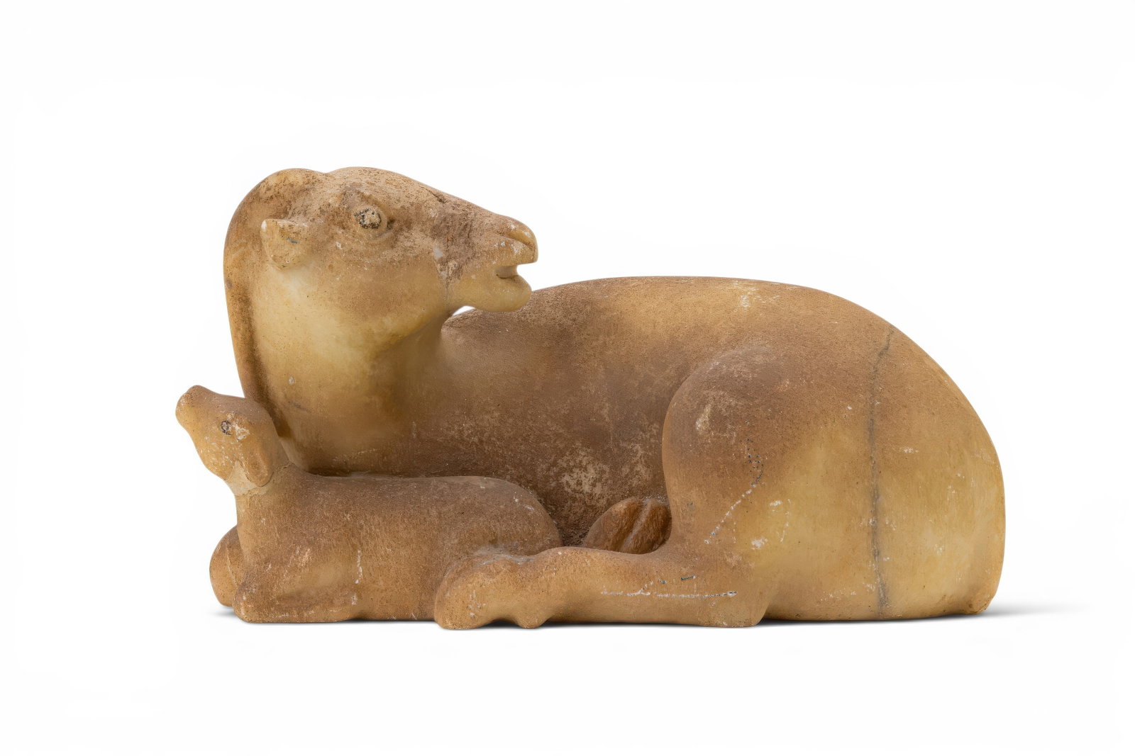 SOUTH ARABIAN MARBLE FIGURINE OF RECUMBENT ANIMALS: Ca. 300 BC. A marble figurine carved as a recumbent animal with a smaller animal resting against its forelegs. The larger figure has a rounded body, folded legs, and an upright neck with the head turn