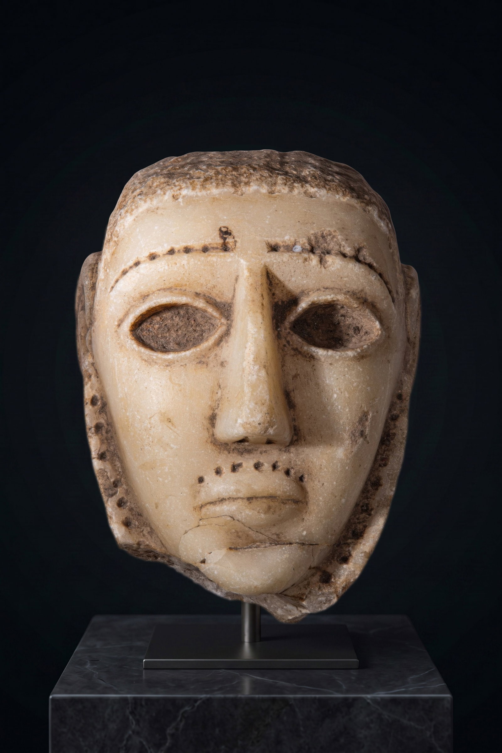 SOUTH ARABIAN ALABASTER HEAD OF A MAN: Ca. 300 - 100 BC. An alabaster head of a man with a broad face, short hair, and large almond-shaped eyes recessed for inlays. The arched brows, moustache, and short beard are marked by rows of drilled