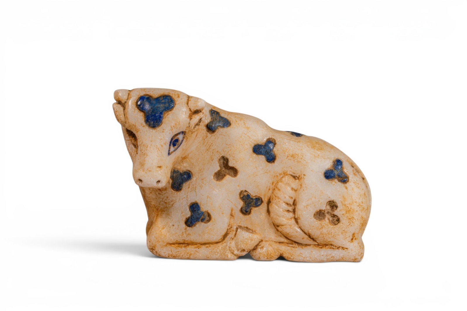 MESOPOTAMIAN MARBLE AND LAPIS LAZULI BULL IDOL: Uruk period, Ca. 3000 - 2500 BC. A marble bull idol carved in recumbent form, with the legs folded beneath the body and the head turned to the side. The face has a long muzzle, almond-shaped eyes, and