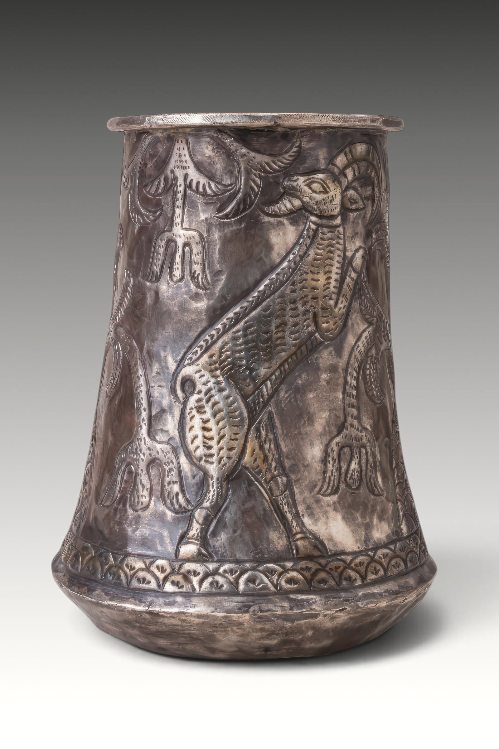 RARE ELAMITE SILVER-GILT BEAKER WITH TREE OF LIFE FLANKED BY RAMPANT STAGS: Ca. 2500 - 1500 BC. A silver-gilt beaker with a rounded lower body, tapering cylindrical wall, and everted rim. The exterior is decorated in relief with a stylised tree of life rising from a scale-pat