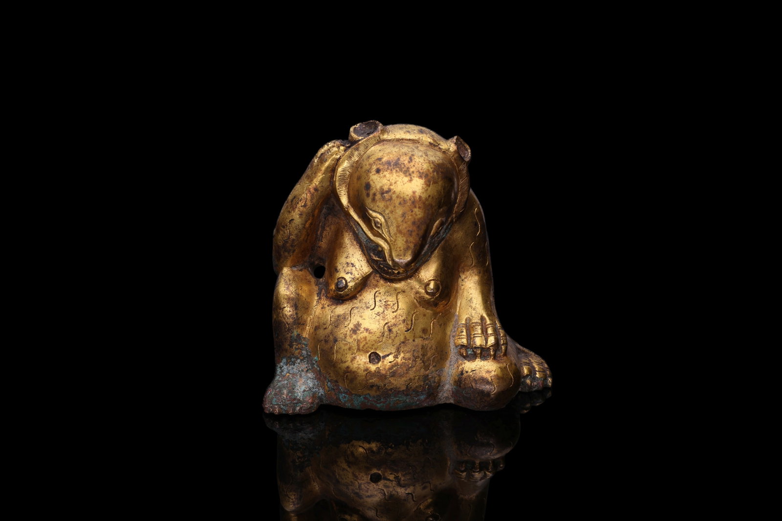 RARE GILT-BRONZE WEIGHT IN THE SHAPE OF A SEATED BEAR: Han Dynasty, Ca. 206 BC - AD 220. A gilt-bronze weight cast as a seated bear with a heavy body and spread hind legs. The head is lowered towards the chest, with rounded ears, almond-shaped eyes and a 