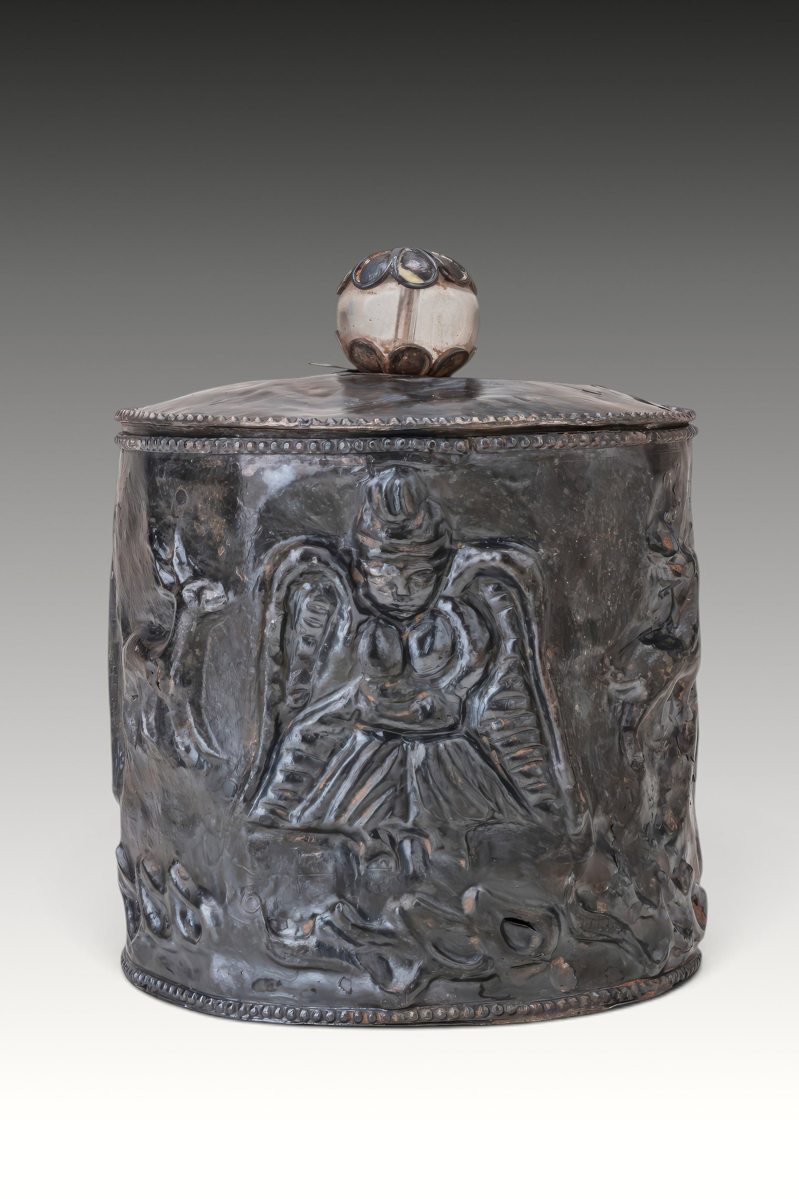 GANDHARAN SILVER PYXIS WITH NIKE-APSARA: Ca. 100 BC - AD 100. A silver pyxis with a cylindrical body and a fitted lid surmounted by a spherical knop set with rosette-shaped mounts of lobed petals. Around the body are winged Nike-Apsara figur