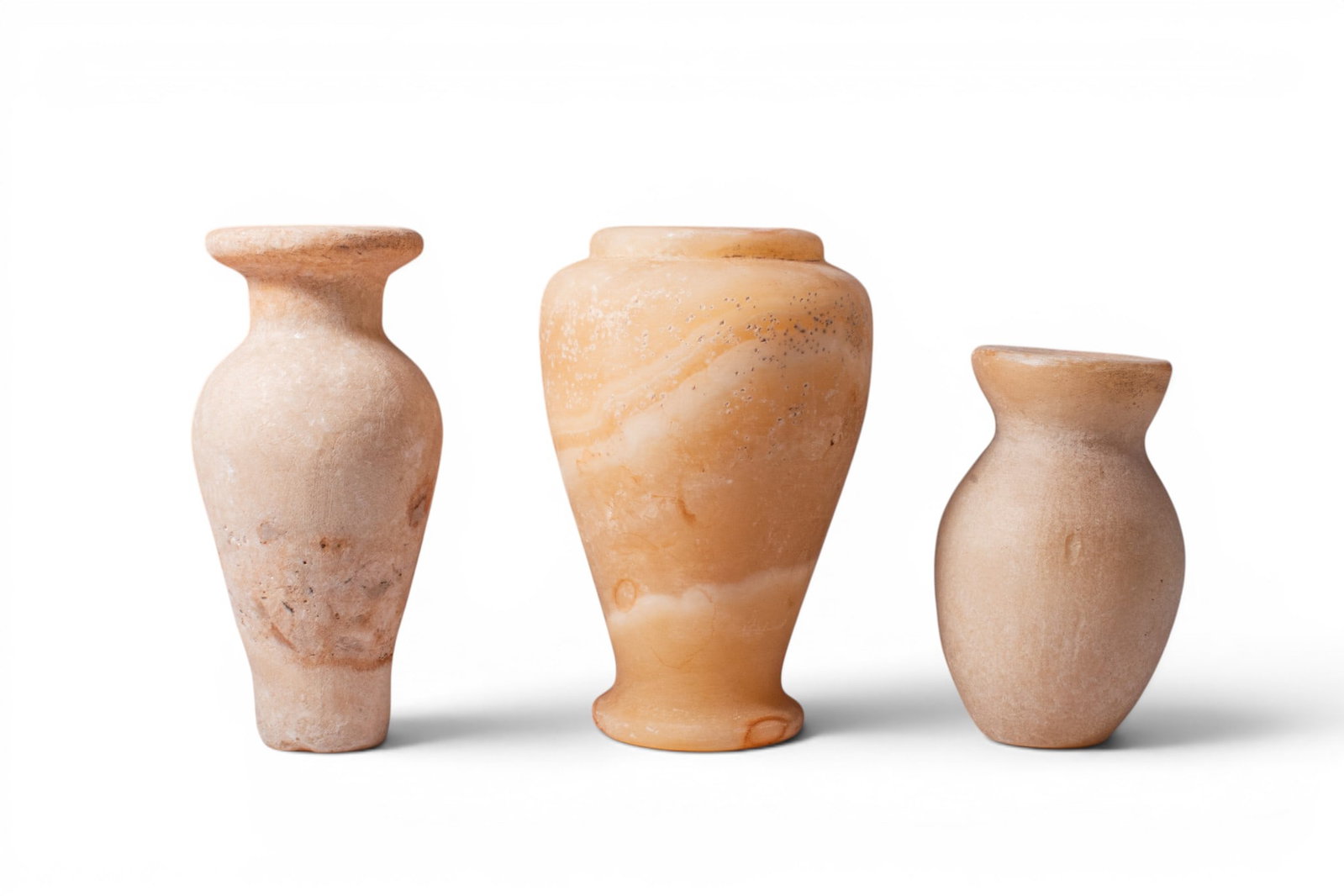 COLLECTION OF EGYPTIAN ALABASTER VESSELS: Old Kingdom, Ca. 2900 - 2640 BC. A collection of three alabaster vessels, including, from left to right: a tall jar with a tapering body, narrow neck, and broad everted rim; a larger jar with a rounde
