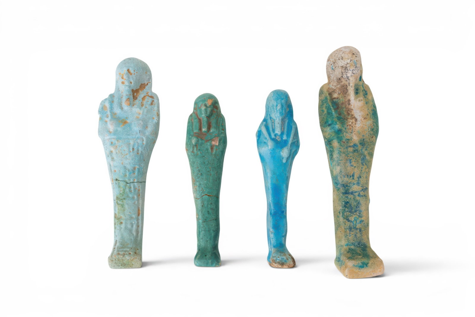 COLLECTION OF EGYPTIAN FAIENCE USHABTIS: New Kingdom to Late Period, Ca. 1550 - 332 BC. A collection of four faience ushabtis, each mummiform with a tripartite wig, false beard, crossed arms, a plain lower body and a dorsal pillar at the bac