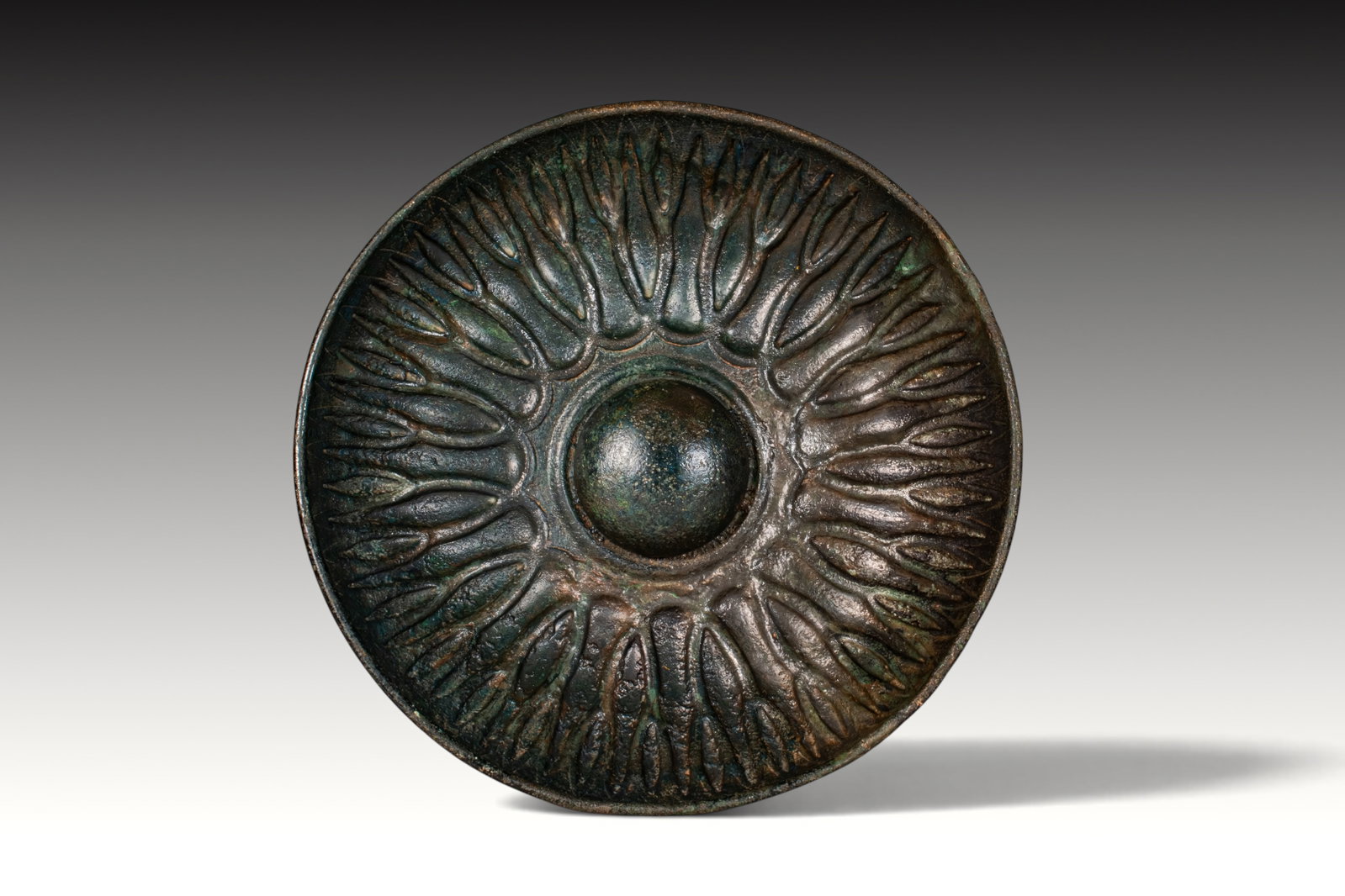 SUPERB GREEK PERIOD BRONZE MESOMPHALOS BOWL: Ca. 500 - 300 BC. A bronze mesomphalos bowl with a shallow rounded body, plain rim, and central raised boss encircled by radiating lotus petals. Size: 200mm x 40mm; Weight: 525g Provenance: Private UK