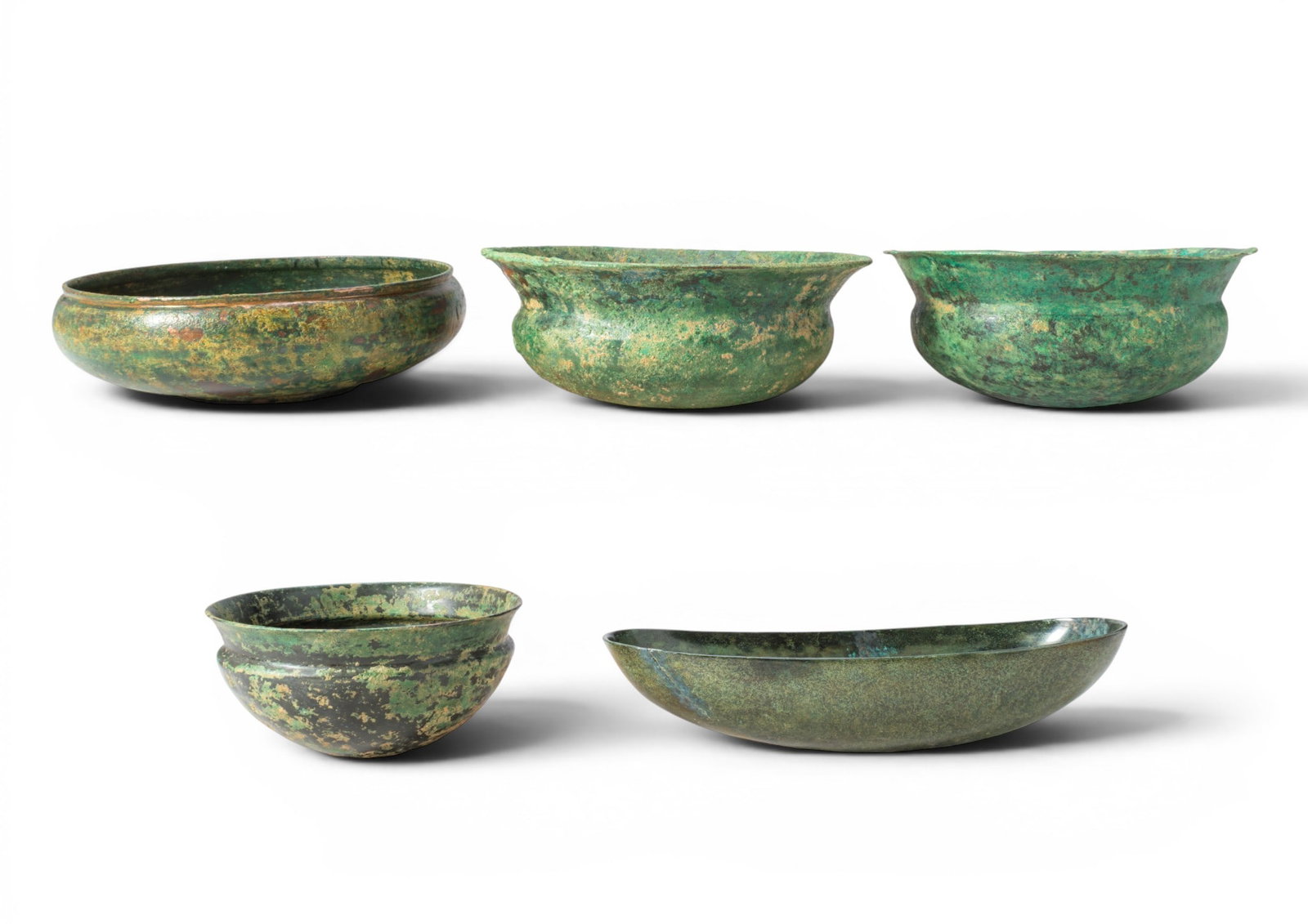 COLLECTION OF ETRUSCAN BRONZE BOWLS: Ca. 500 - 300 BC. A collection of five bronze bowls, including, from left to right: a shallow bowl with an upright rim; three bowls, each with a flaring rim above a carinated shoulder; and an elongate