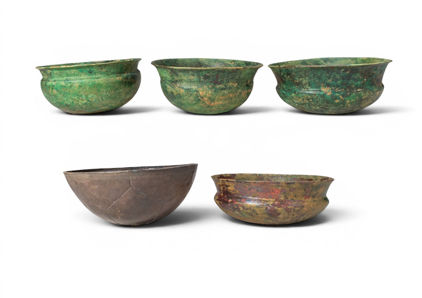 COLLECTION OF ETRUSCAN BRONZE BOWLS: Ca. 500 - 300 BC. A collection of five bronze bowls, including: four bowls, each with a rounded body, flaring rim, and carinated shoulder; and a deeper bowl with incised geometric panels below the orn