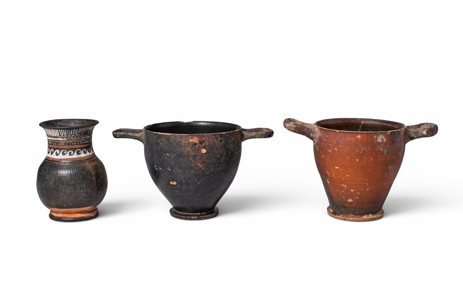 COLLECTION OF APULIAN VESSELS: Ca. 400 - 300 BC. A collection of three vessels, including, from left to right: a Gnathian mug with a ribbed globular body, loop handle, flaring neck, and bands of white, ochre, and red ornament; and 