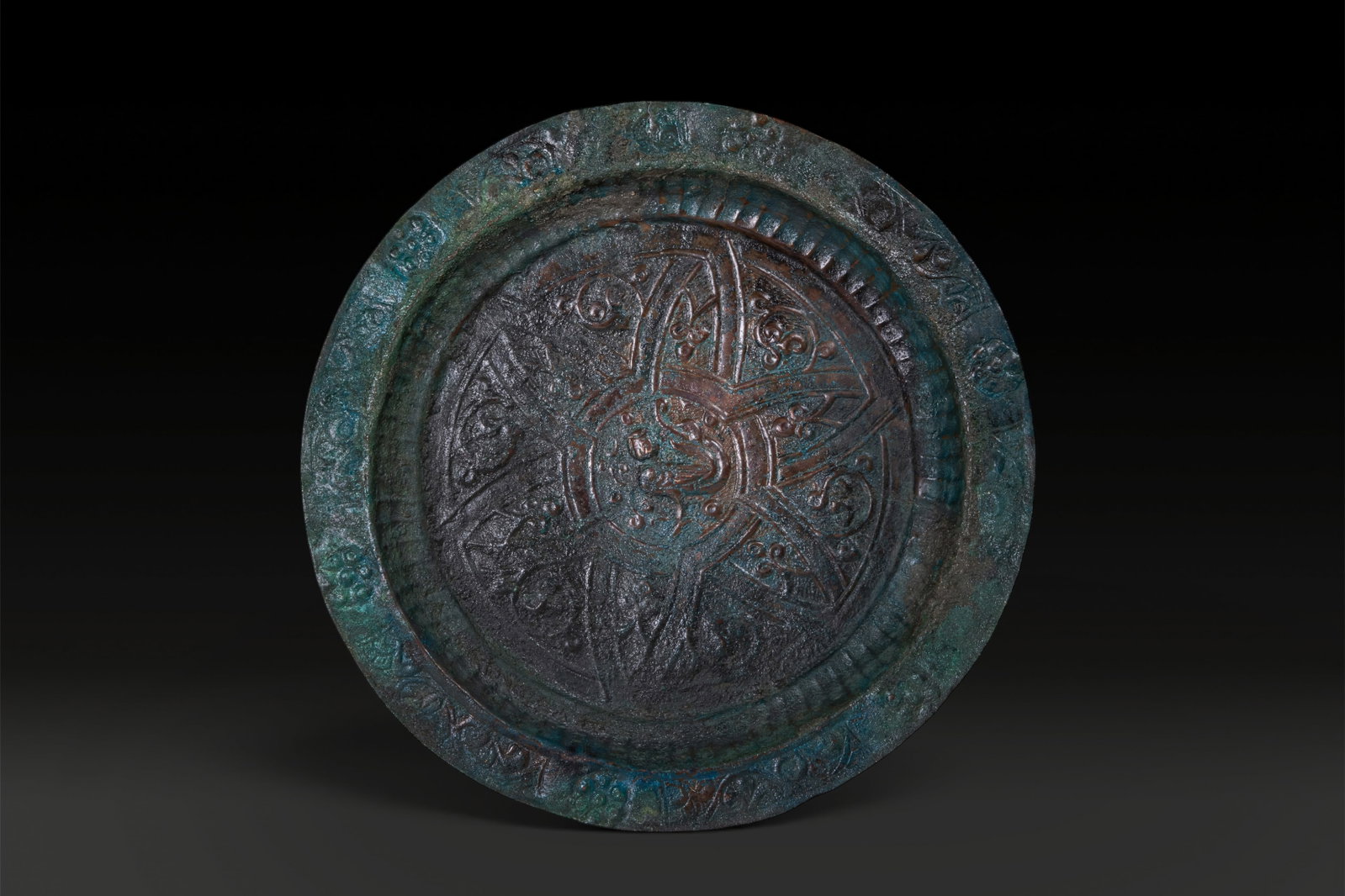 RARE SELJUK BRONZE SHALLOW BOWL WITH SIREN: Ca. AD 1000 - 1200. A shallow bronze bowl with a broad everted rim and a fluted cavetto. The centre is decorated in relief with a siren in profile, surrounded by radiating geometric and foliate panels