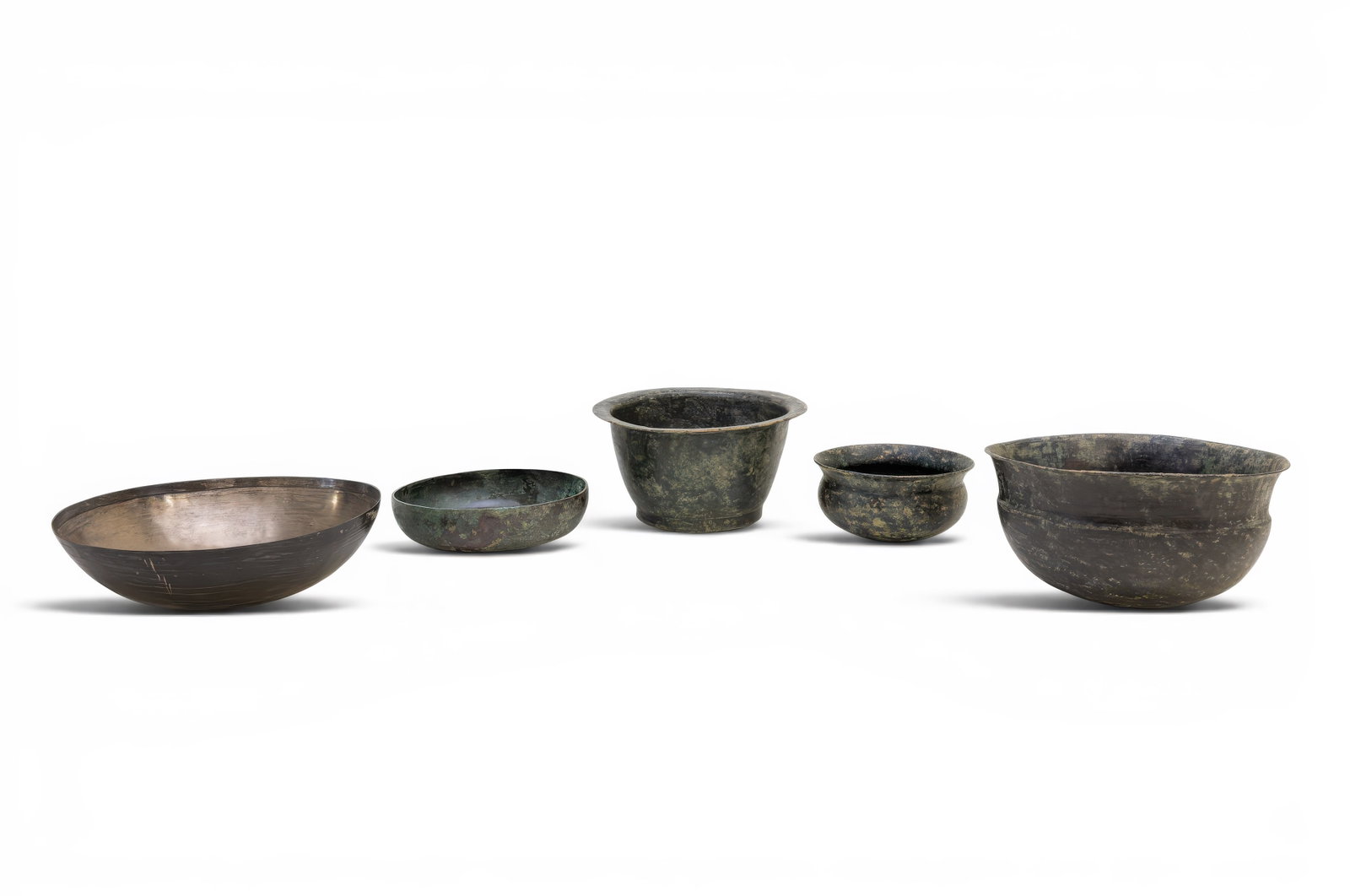 COLLECTION OF GREEK BRONZE BOWLS: Ca. 500 BC. A collection of five bronze bowls, including, from left to right: a broad shallow bowl with a rounded body and straight rim; a low bowl with a compressed body; a deep bowl with tapering si
