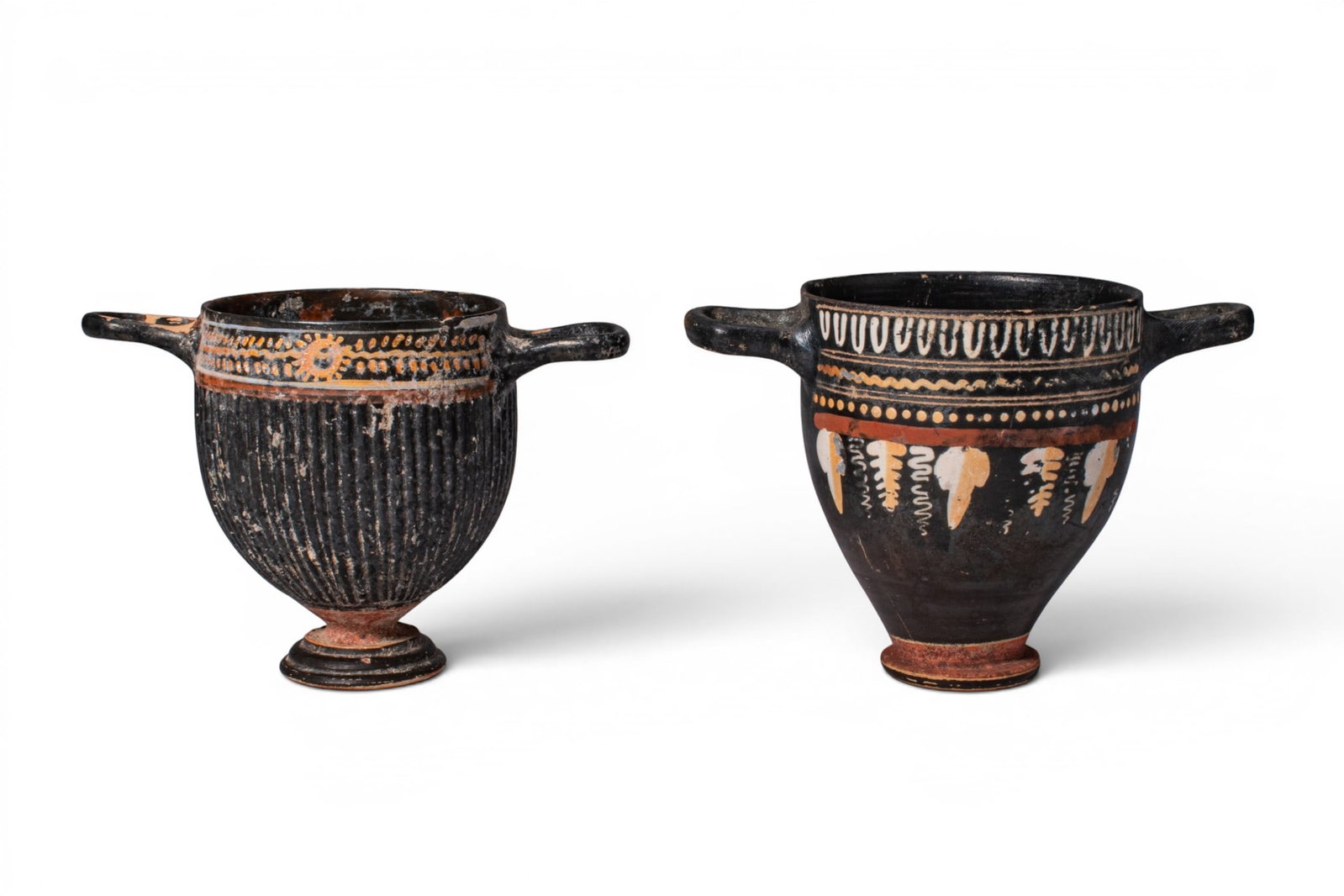 PAIR OF GREEK GNATHIAN POTTERY SKYPHOI: Ca. 325 - 275 BC. A pair of skyphoi, each with a deep body, twin horizontal handles, a short foot, and a plain rim. The example on the left has a ribbed lower body below bands of added white, ochre, a