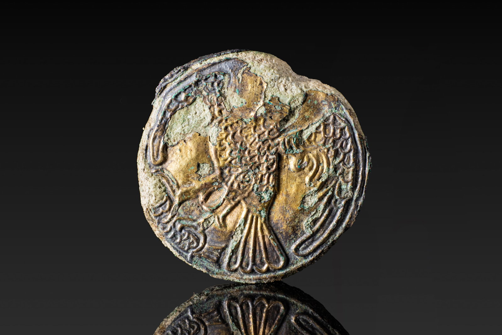 ROMAN GOLD LEAF AND BRONZE SEAL WITH STANDING EAGLE: Ca. AD 1 - 300. A bronze seal with a circular face overlaid in gold leaf, depicting a standing eagle with outspread wings. The body is rendered with dense feathering, with the head turned to the side