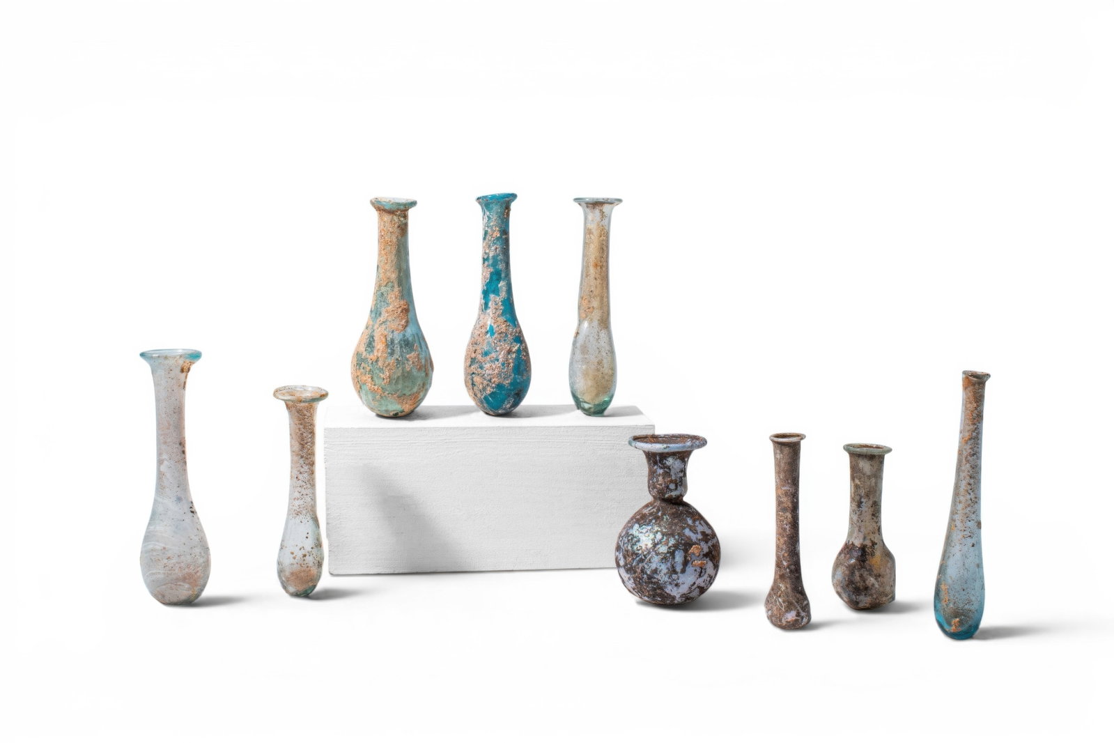 LARGE COLLECTION OF ROMAN GLASS UNGUENTARIA: Ca. AD 1 - 300. A collection of nine glass unguentaria, including, from left to right: five slender flasks with elongated pear-shaped bodies, long necks, and flared mouths; a squat flask with a
