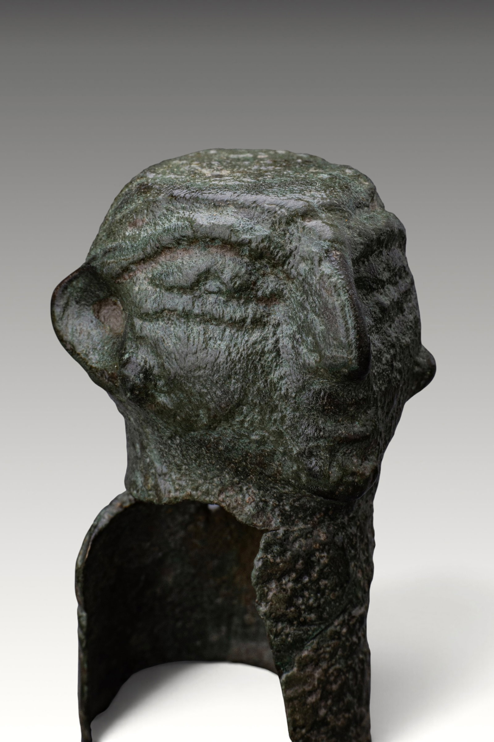 CELTIC BRONZE ANTHROPOMORPHIC FITTING: Ca. 200 BC - AD 100. A bronze anthropomorphic fitting with a broad stylised head above an elongated neck. The face has a prominent nose, large eyes, and a narrow mouth, with the ears projecting at