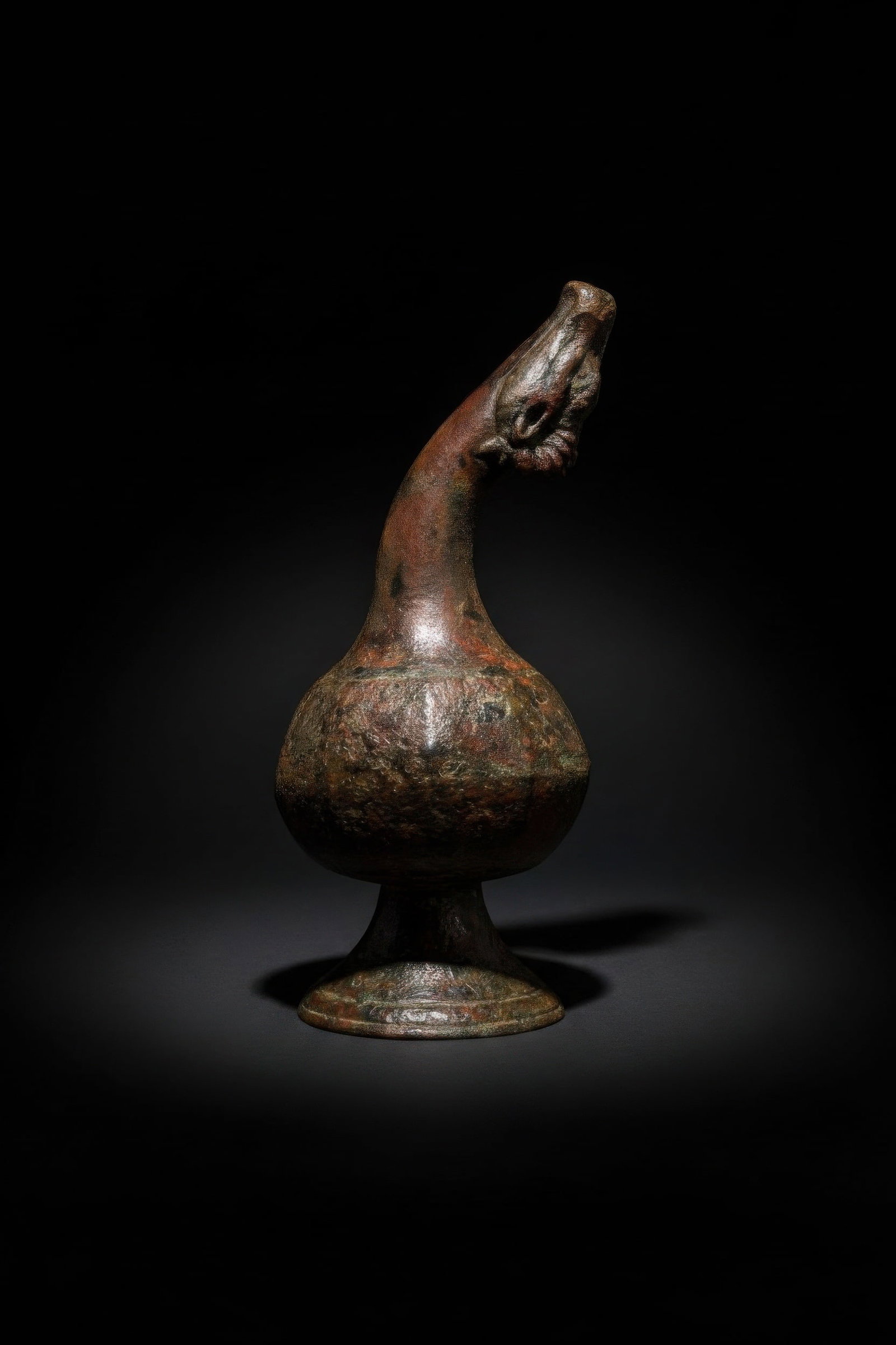 SOUTH INDIAN BRONZE DRIPPING VESSEL (THARA PATHIRAM) WITH COW-HEAD SPOUT: Ca. AD 1700 - 1800. A bronze thara pathiram, a dripping vessel with a bulbous body on a flared foot and a tall arched neck. The spout is modelled as a cow’s head, with incised eyes, muzzle, ears and