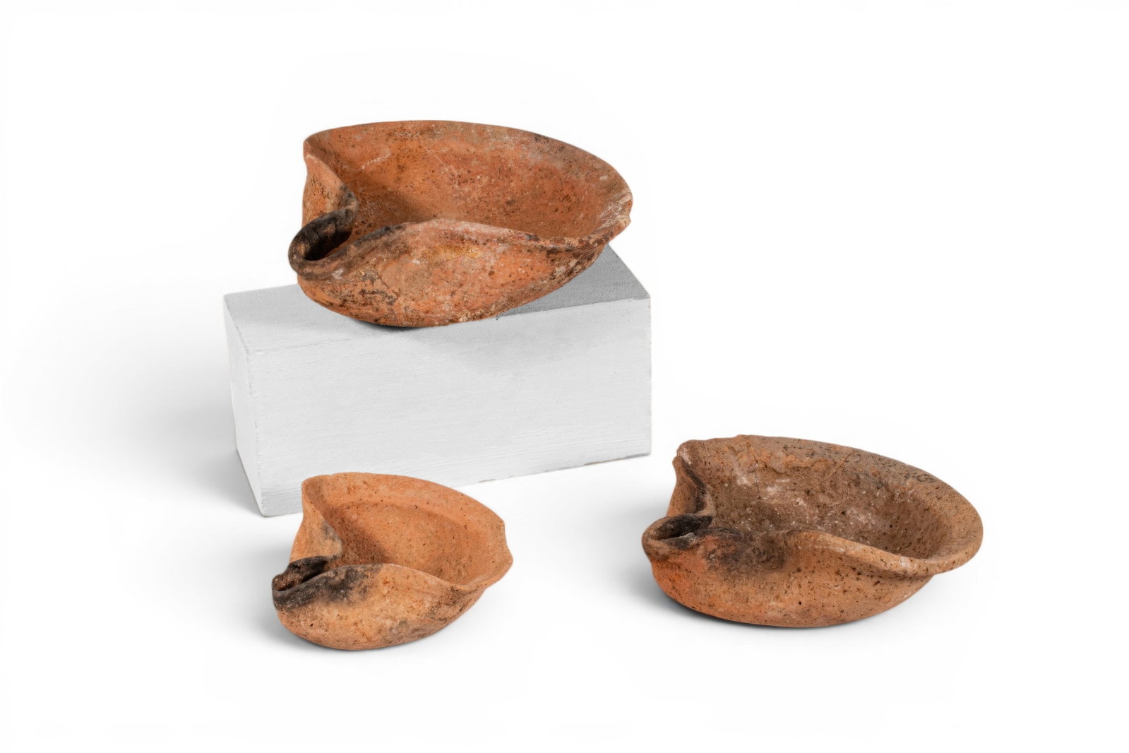 COLLECTION OF IRON AGE HOLY LAND TERRACOTTA OIL LAMPS: Ca. 800 - 500 BC. A collection of three terracotta oil lamps, each of Vessberg Type 1, with a shallow rounded body, broad open basin, and pinched nozzle. The rims are folded inward to frame the fillin