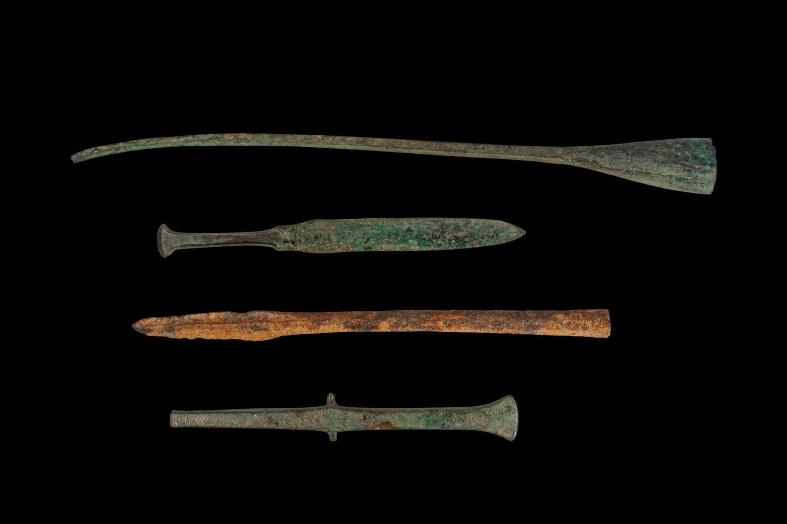COLLECTION OF BRONZE AGE / EARLY GREEK PERIOD BRONZE BLADES: Ca. 1200 - 800 BC. A collection of four bronze blades, including, from top to bottom: a long narrow blade with a slightly curved profile, expanding to a flaring socket; a dagger with a long blade, fla
