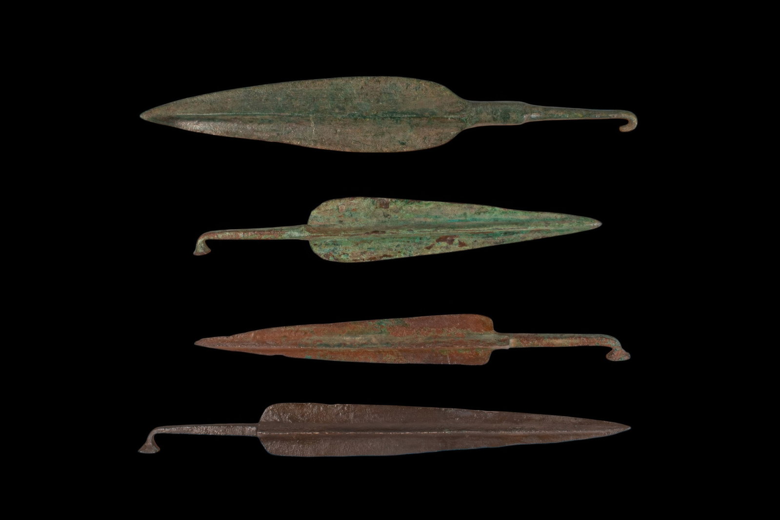 COLLECTION OF BRONZE AGE / EARLY GREEK PERIOD BRONZE DAGGERS AND SPEARHEADS: Ca. 1200 - 800 BC. A collection of four bronze daggers and spearheads, including, from top to bottom: a leaf-shaped dagger with a broad blade, central rib, and hooked tang; a spearhead with a midrib a
